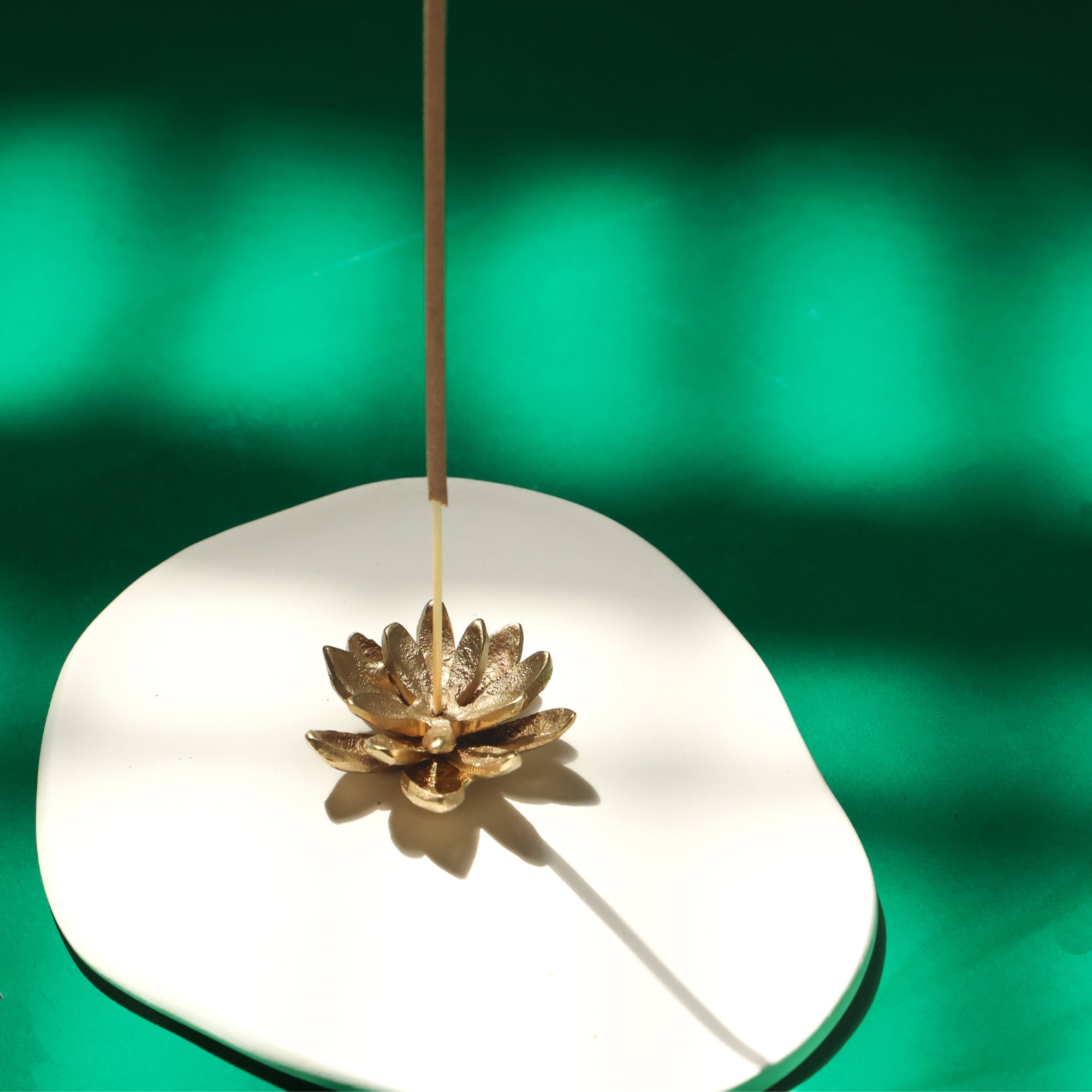 Gold lotus-shaped incense burner on a white base with a green background