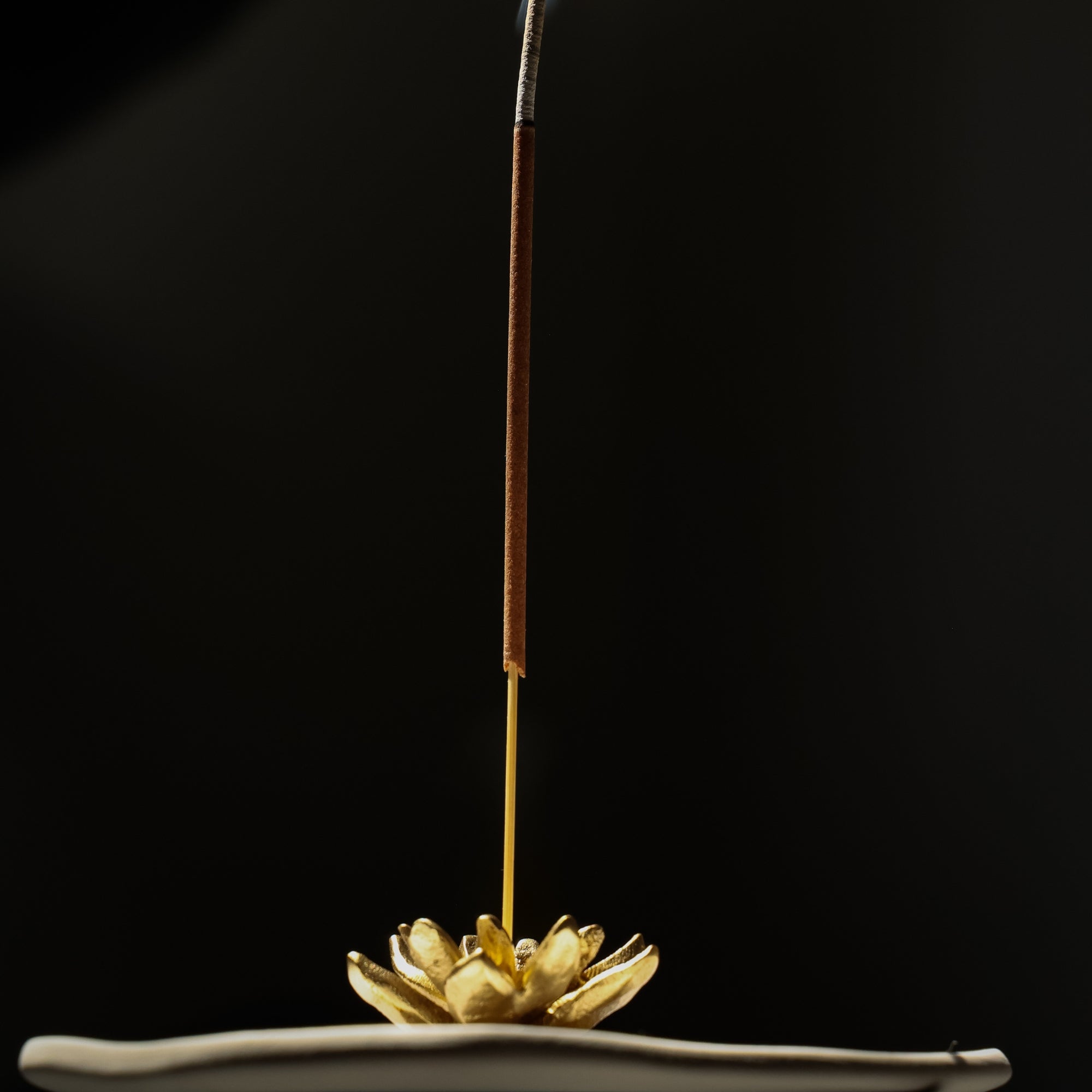 Incense stick on a lotus-shaped holder against a black background