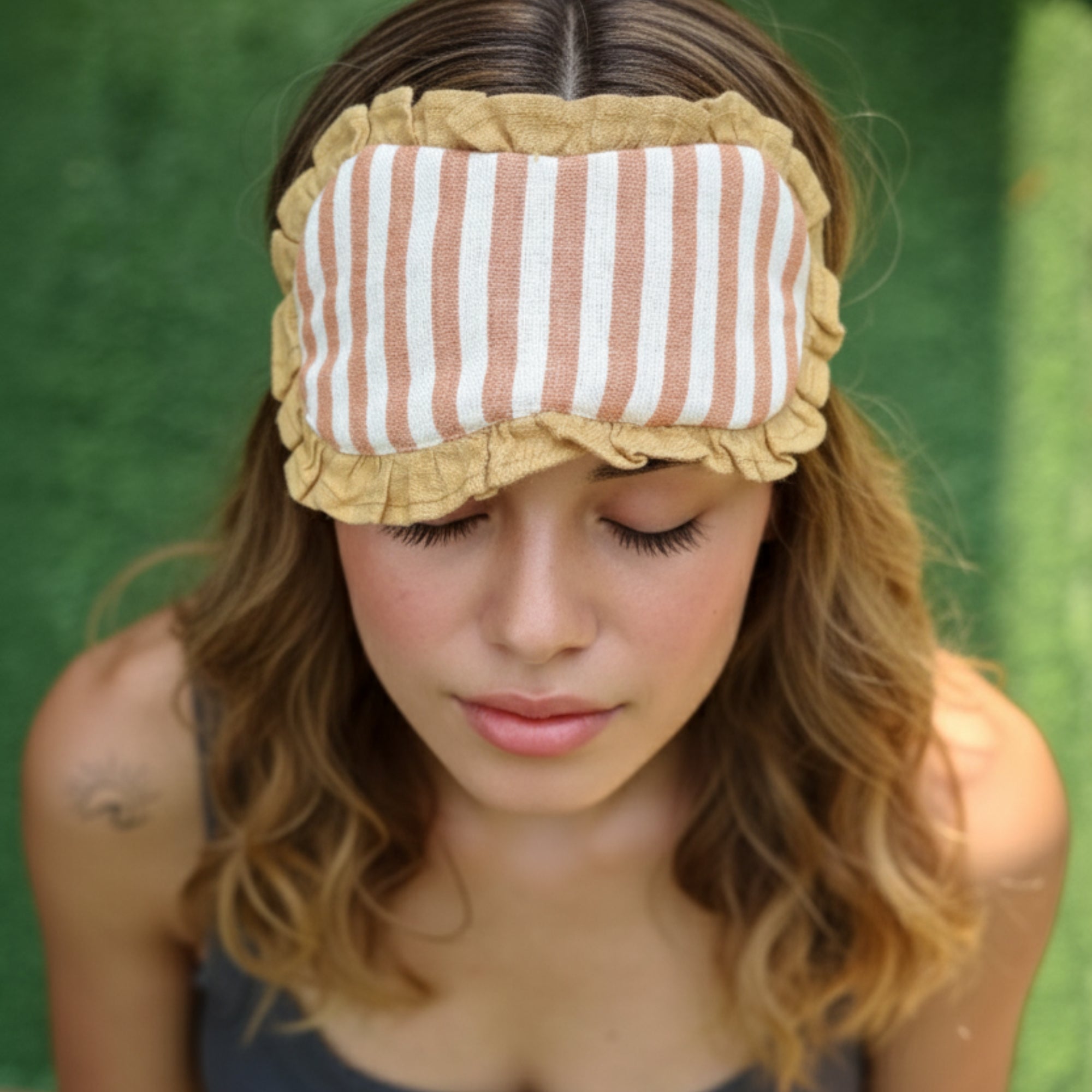 Woman wearing a striped linen fabric eye mask with ruffles against a green background