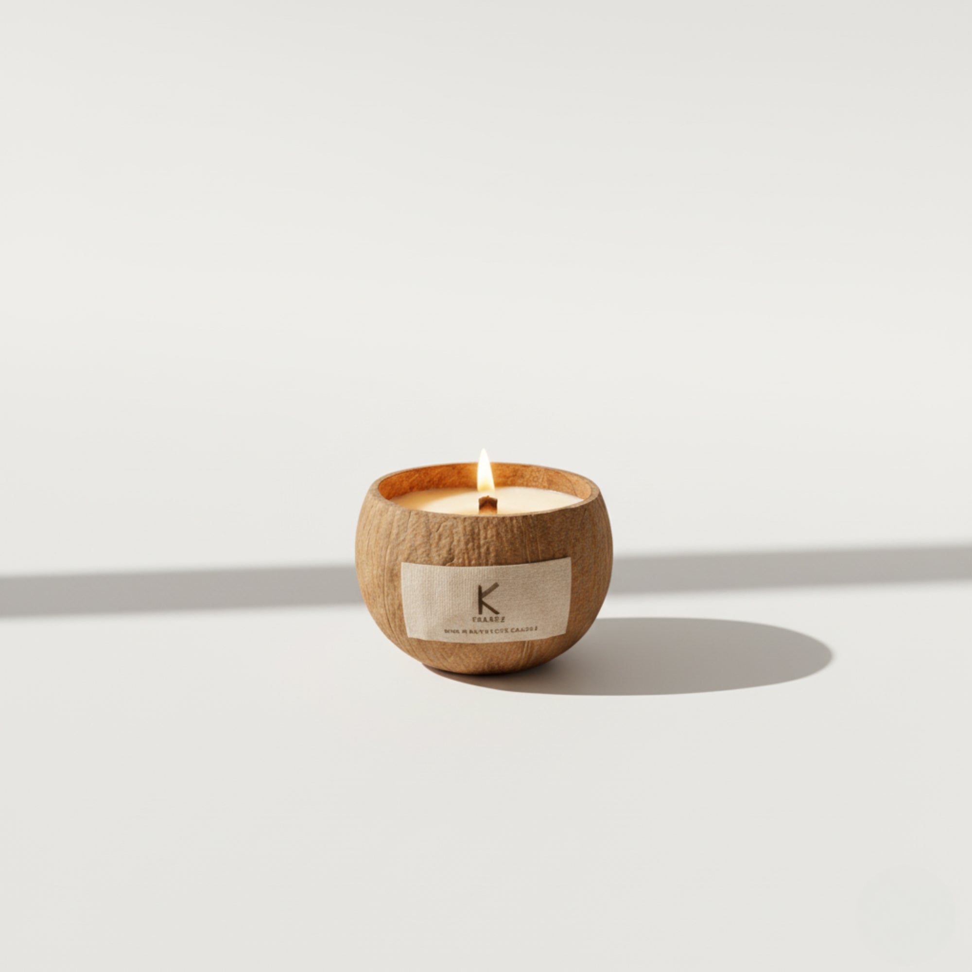 Candle in a coconut shell with a visible brand 'K' label on a light background