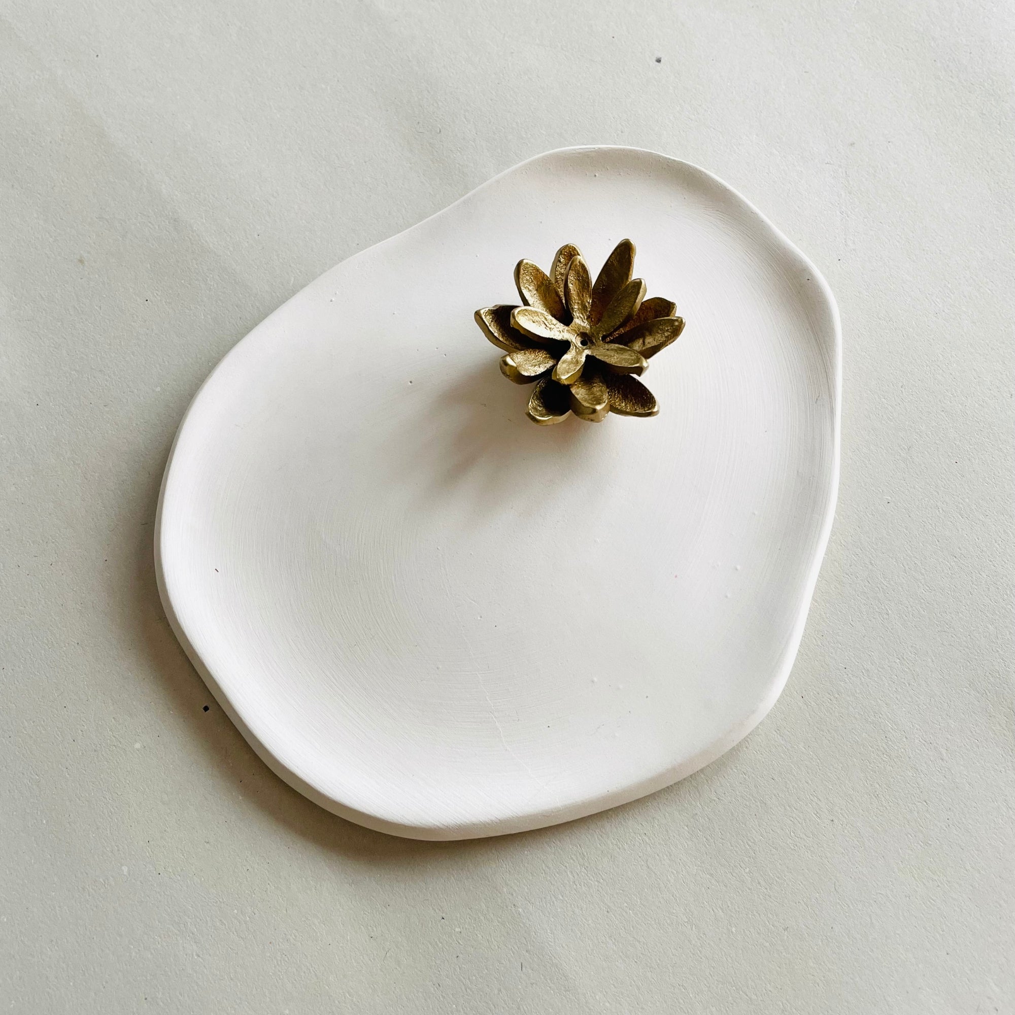 A gold-colored brass incense holder with a lotus design on a white ceramic ash-catcher tray.