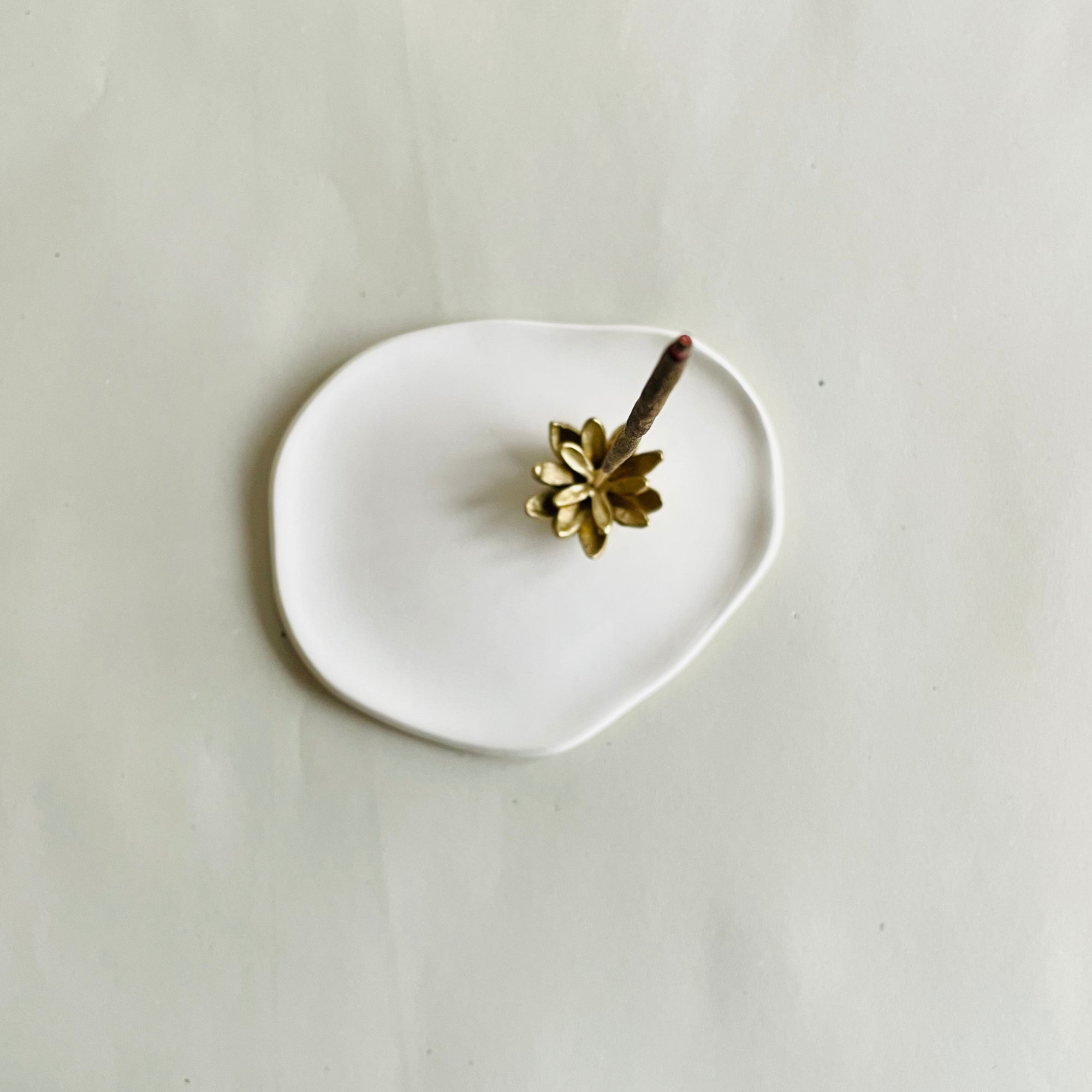 Incense stick burn on a brass lotus shaped incense holder attached to a ash catcher tray placed against a white backdrop.