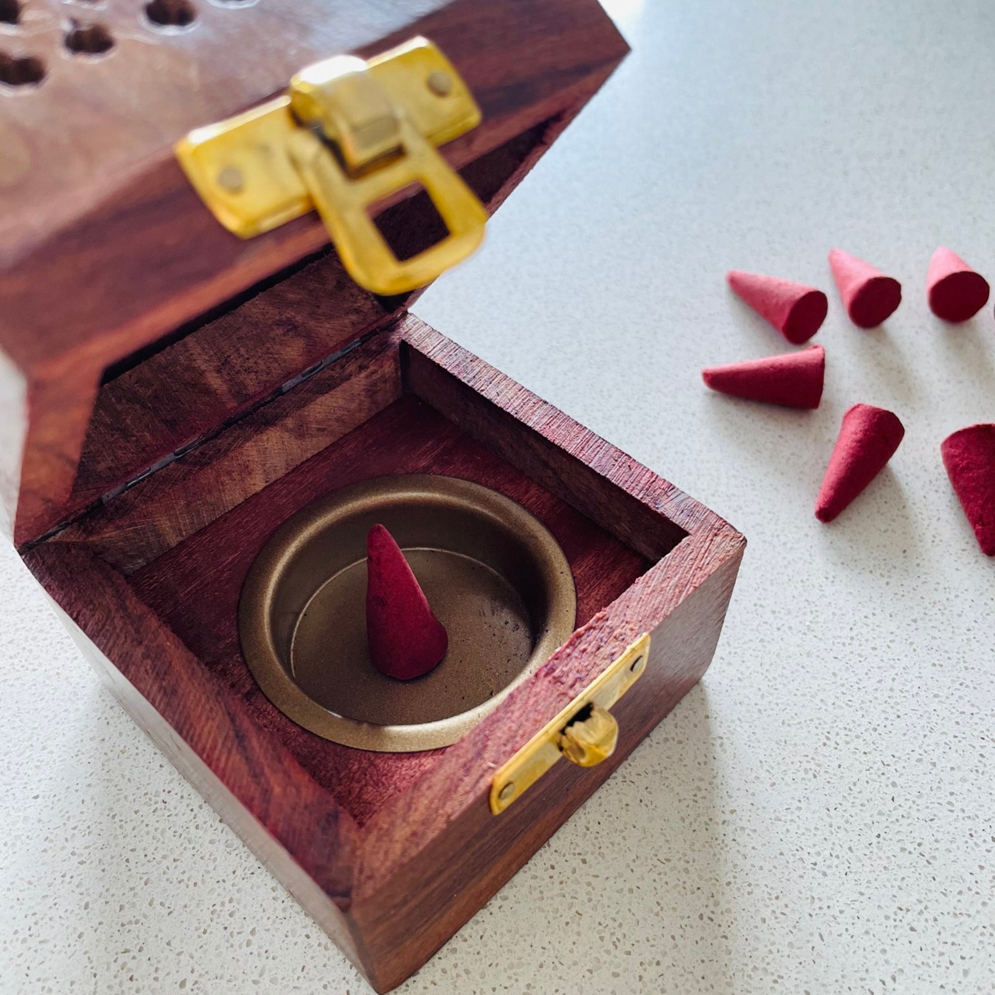 Wooden incense burner containing a red cone with cinnamon fragrance surrounded by more red cones on a dark surface.