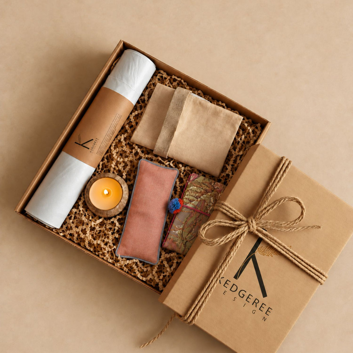 A curated Yogi Gift set by Kedgeree Design includes a yoga mat, candle, eye pillow, journal, yoga bag and a gift box on a brown background.