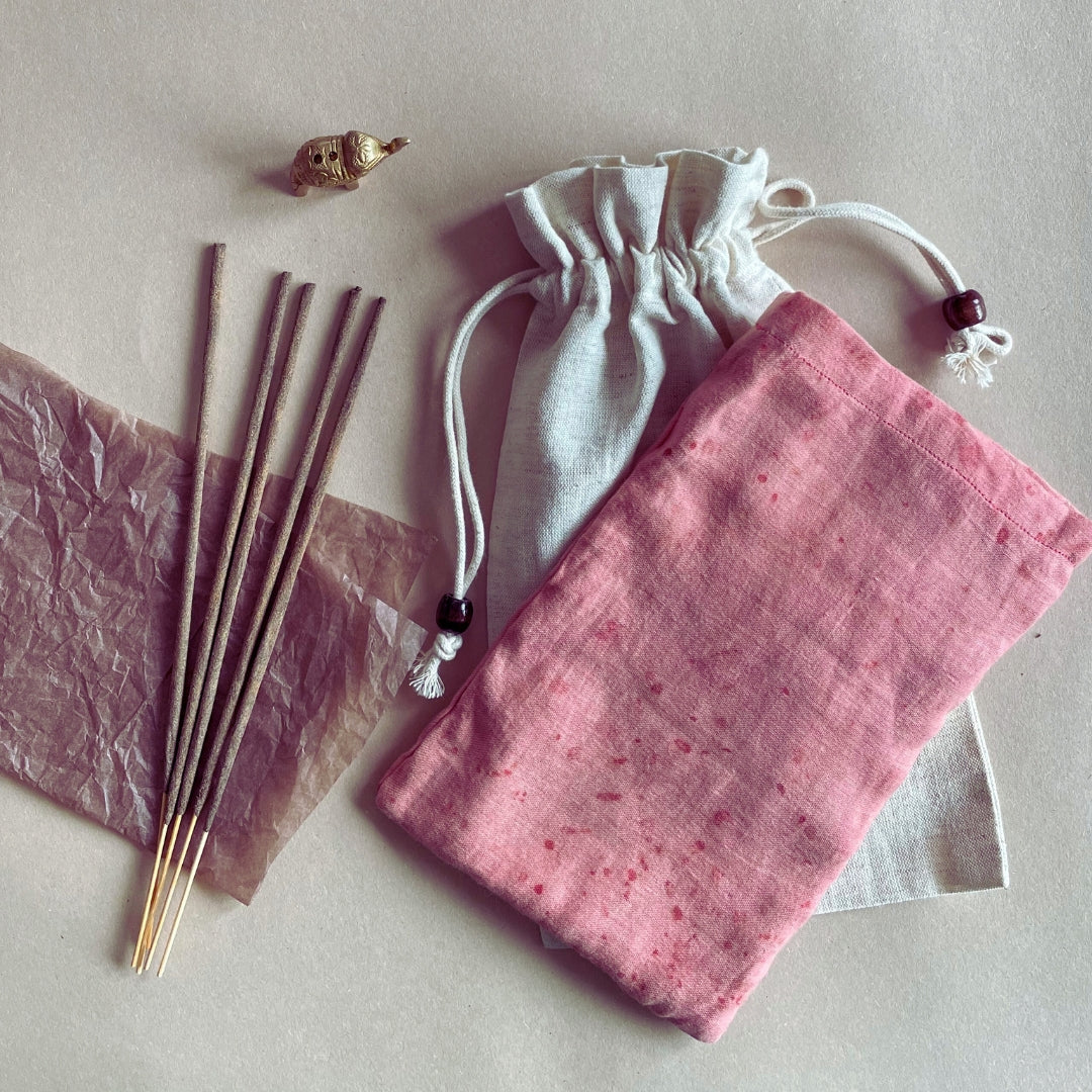 A collection of eye pillows in various states of use, including one with a pink pattern, one with a beige fabric, and several sticks with essential oil drops on them, all placed on a neutral background.