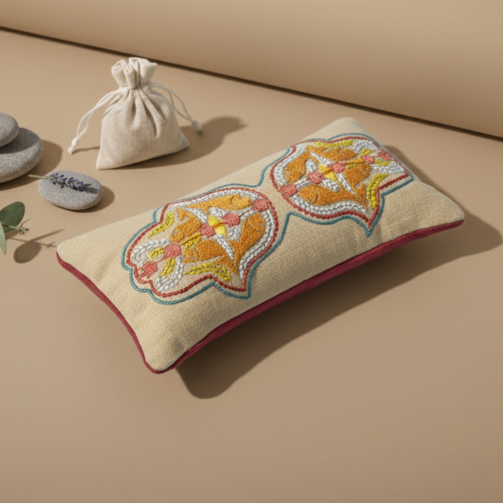 Decorative eye pillow with floral embroidery on a beige surface, accompanied by a small drawstring bag and stones.