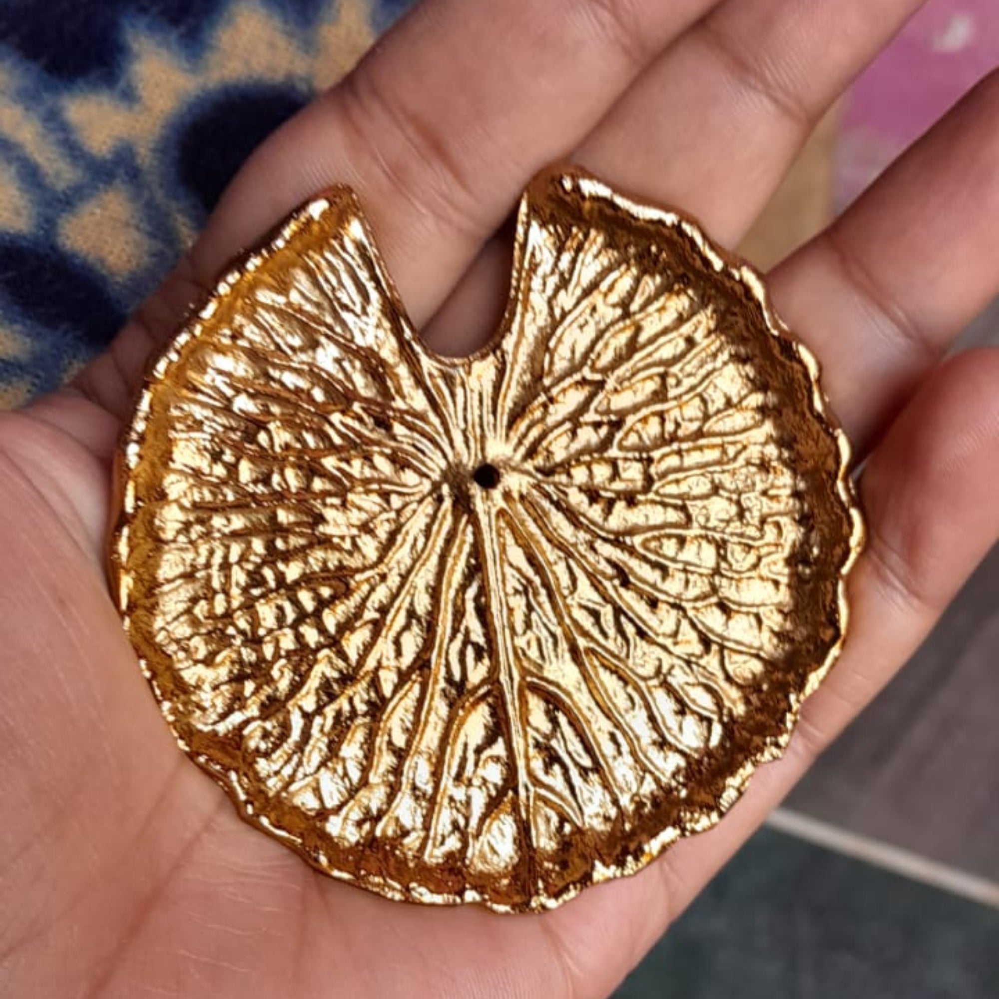 Gold leaf-shaped brass incense holder object held in a hand with a blurred background