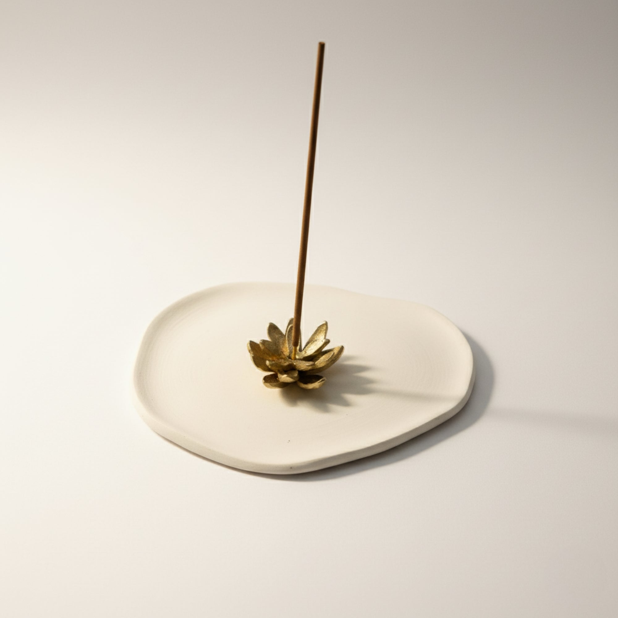 Brass incense holder with a single incense stick on a light gray background
