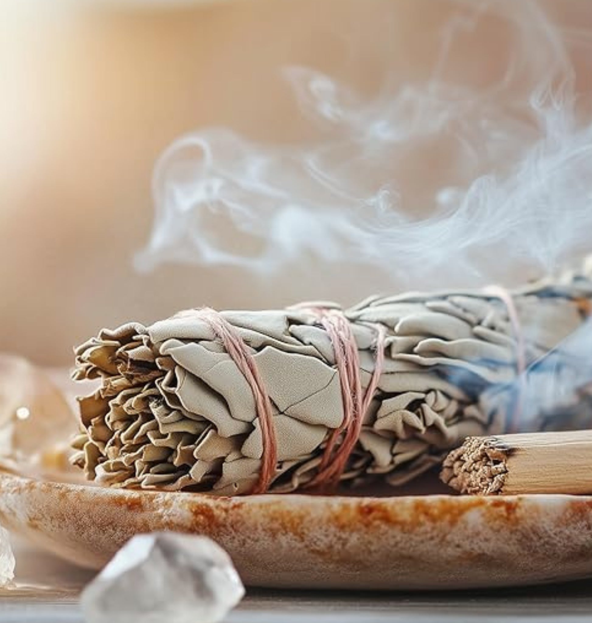 Hand-wrapped aromatic white sage smudge sticks tied with cotton string, smouldering in a fire-safe dish for home energy cleansing.