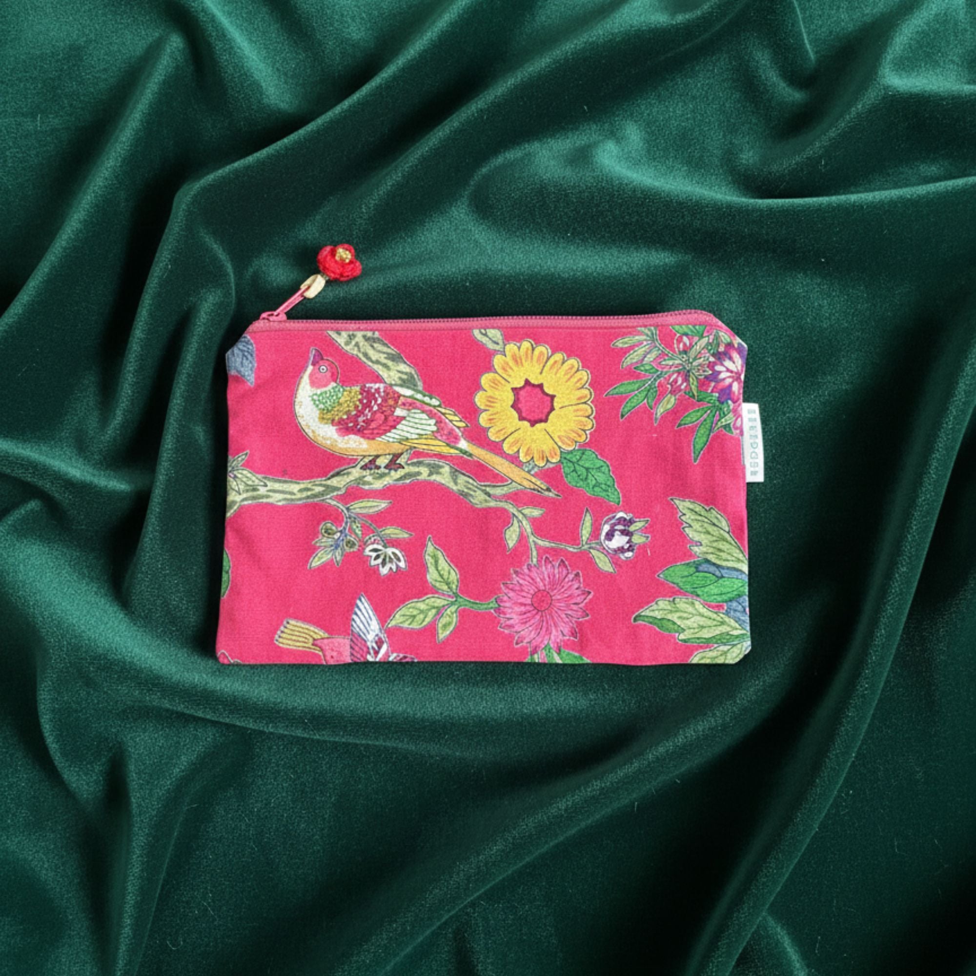 Red travel pouch with floral and bird design on a green fabric background