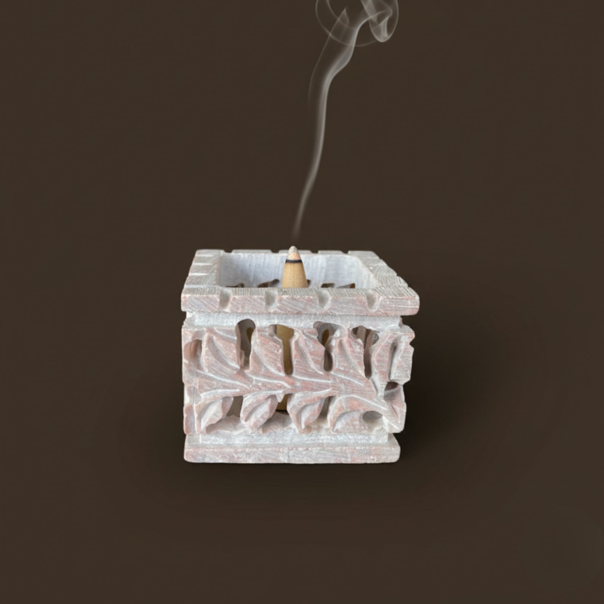Decorative incense burner with a lit incense cone on a dark background