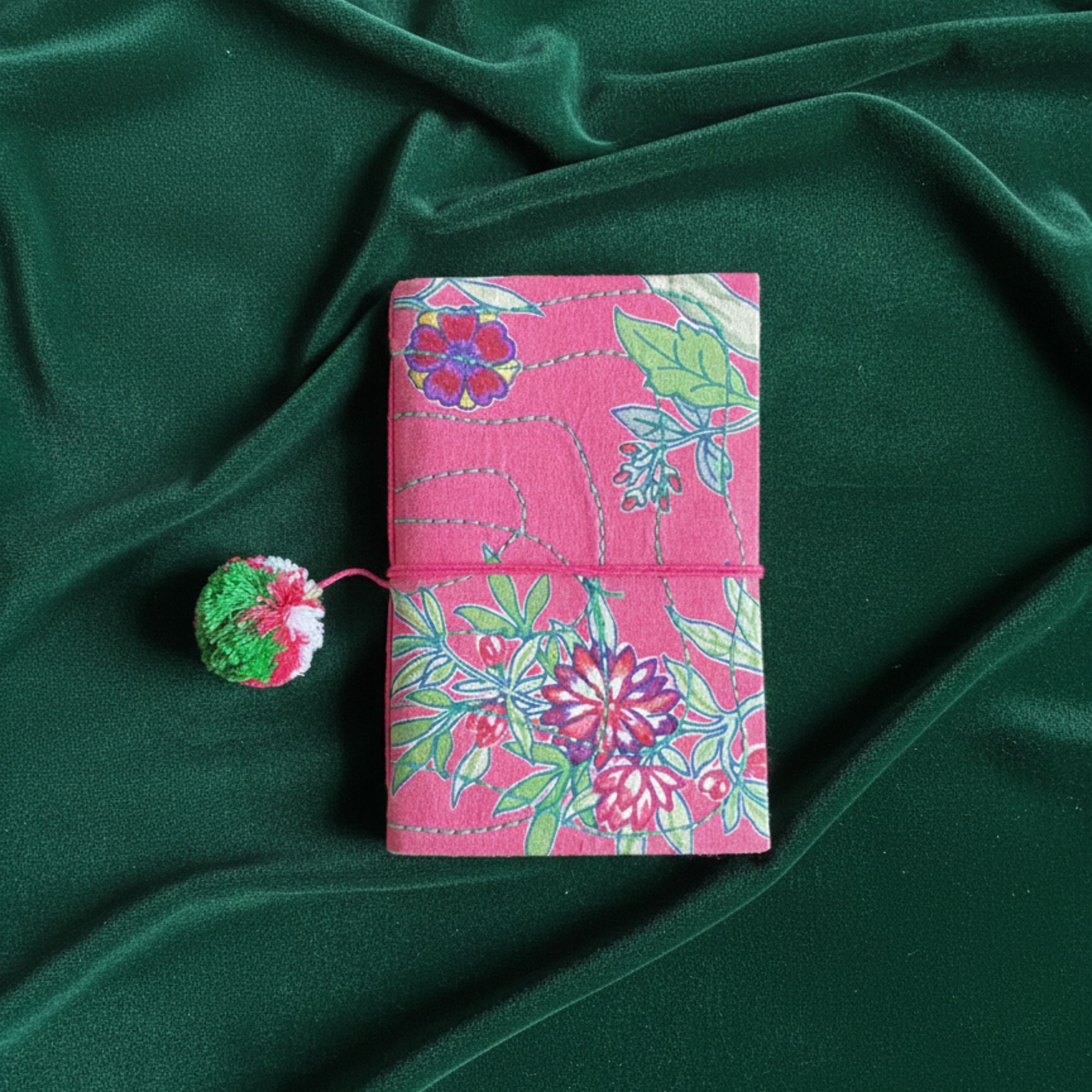 Floral red journal with a green pom-pom on a green fabric background