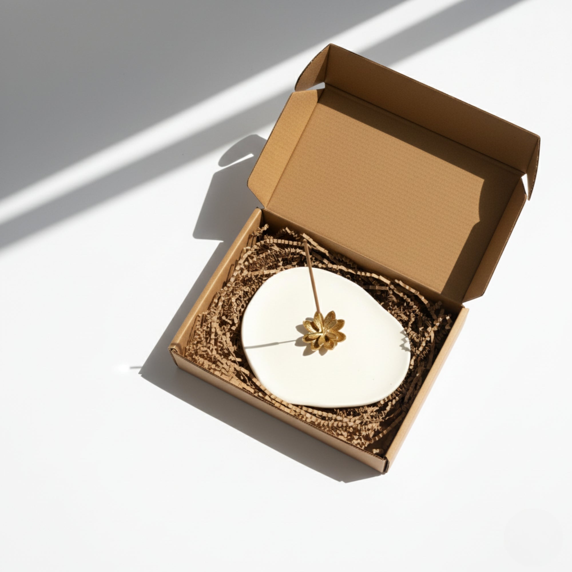 Open giftbox with a gold colour handmade brass lotus incense holder on a light background