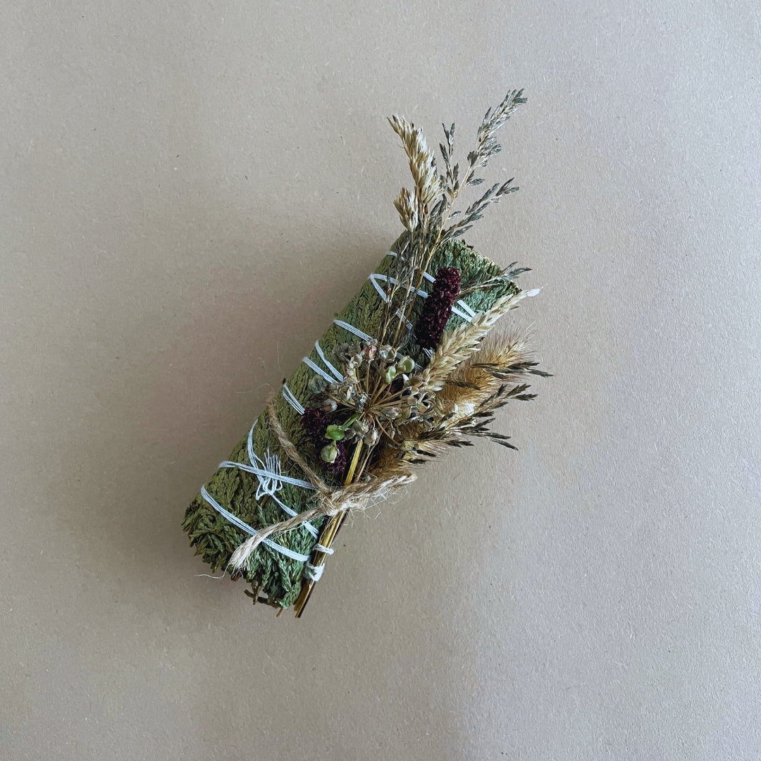 Handcrafted cedar smudge stick with dried flowers in a handmade pouch, slow-burning for home cleansing rituals.