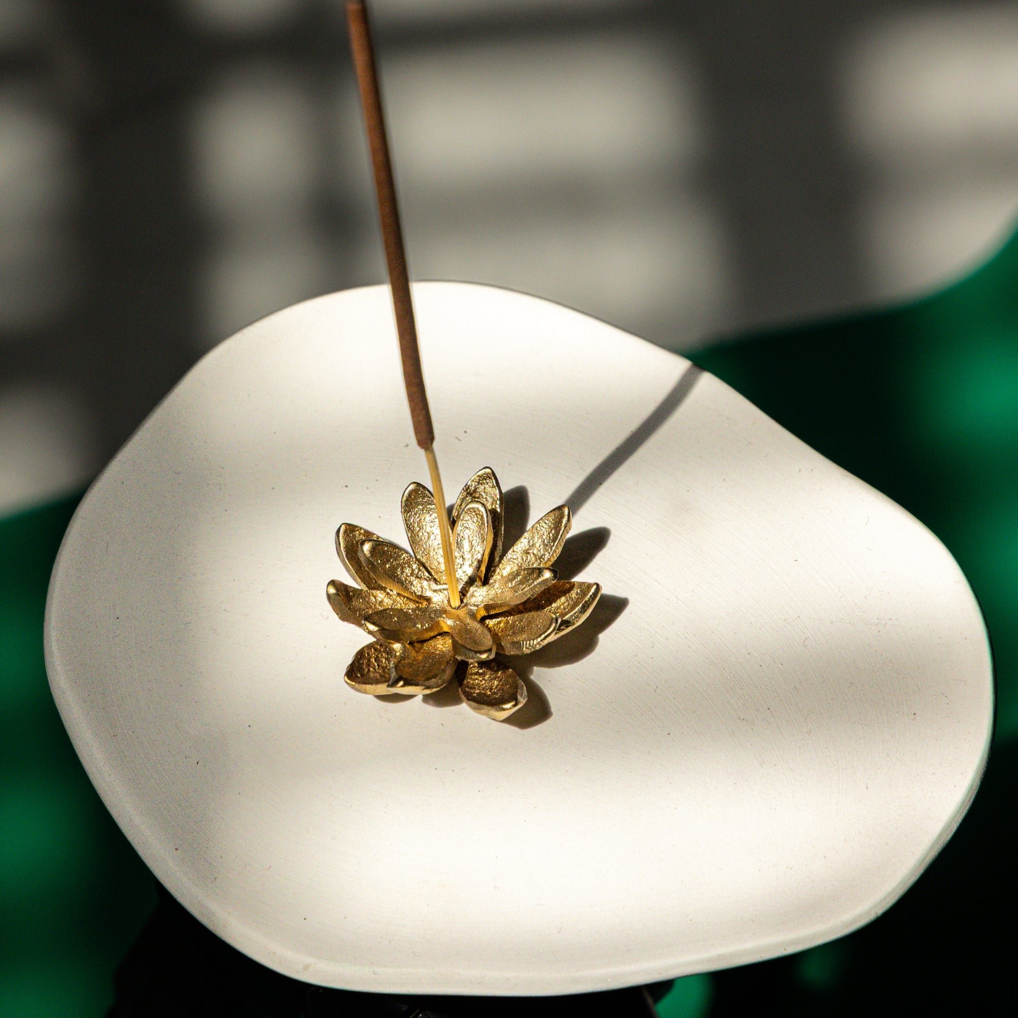 Gold incense burner shaped like a lotus flower on a white plate with a blurred green background