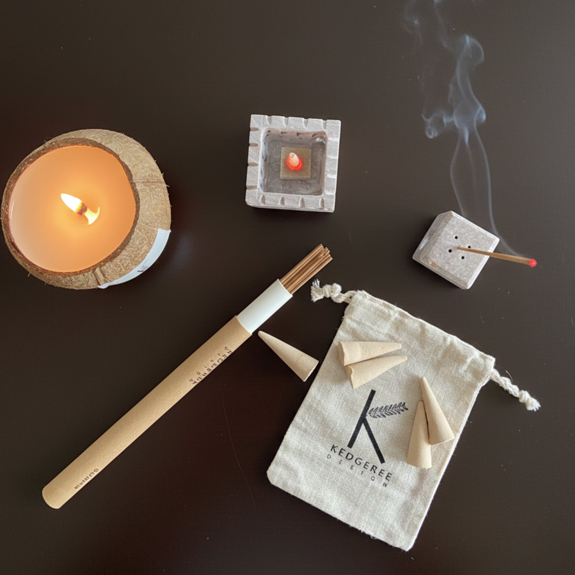 Natural Candle, hand rolled incense sticks, and cones on a dark surface with smoke