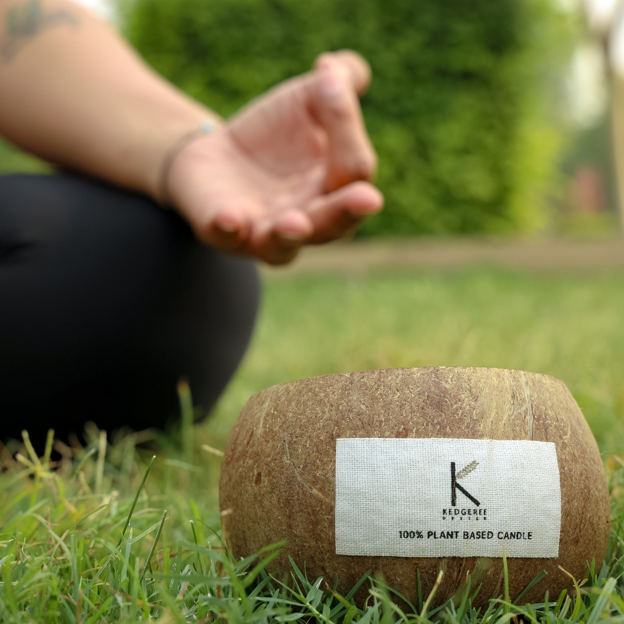 Plant based coconut shell morning meditation candle lit in the forground and a person doing yoga in the background
