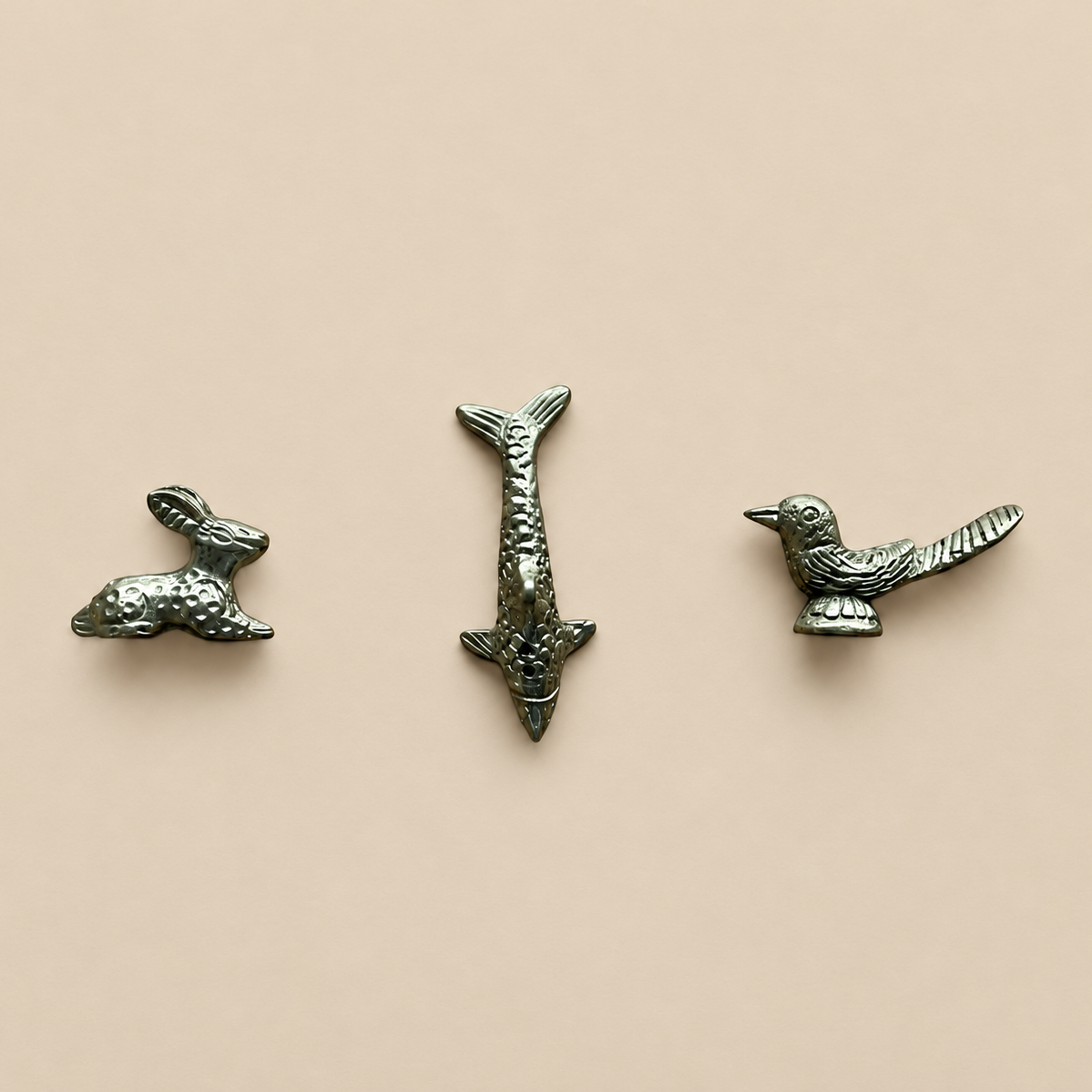 Three brass animal shaped hare, fish and bird incense holder figurines on a brown background
