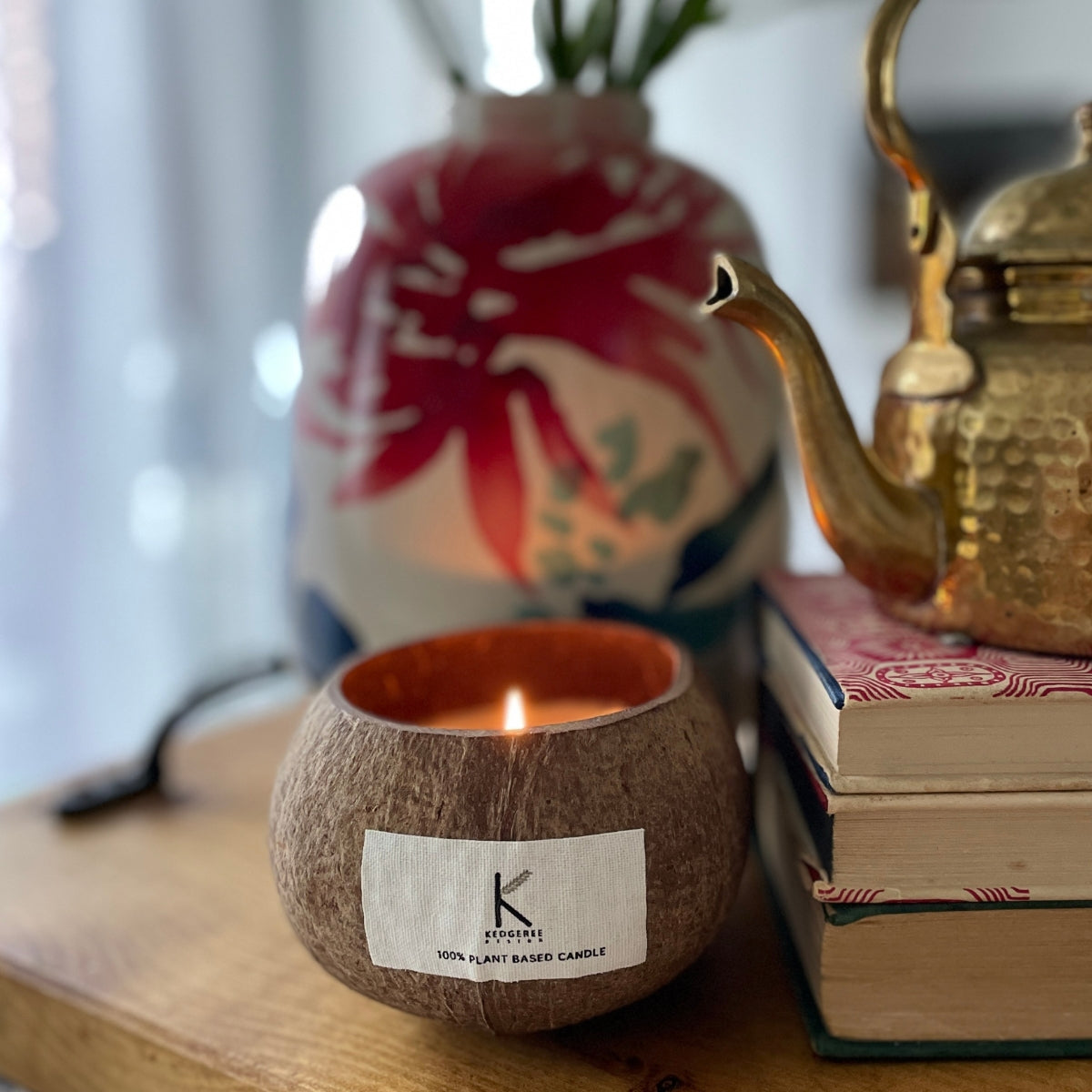 Plant Based Candle in a coconut shell with a visible brand label, books, and a decorative vase in the background.