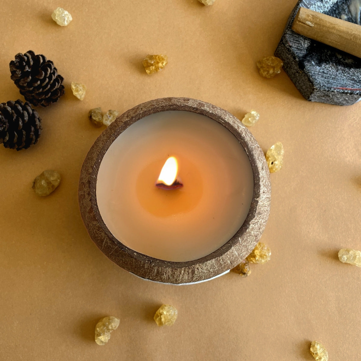 Plant Based Coconut Shell Candle lit on the foreground with decorative elements on a beige background