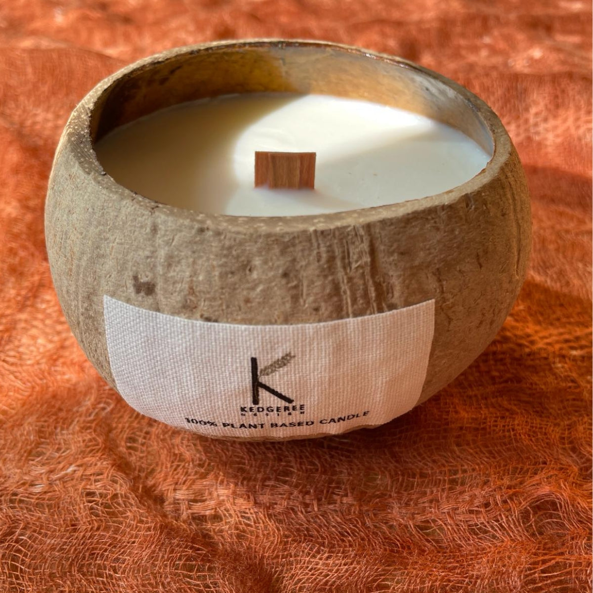 Plant Based Candle in a coconut shell with a wooden wick on an orange fabric background