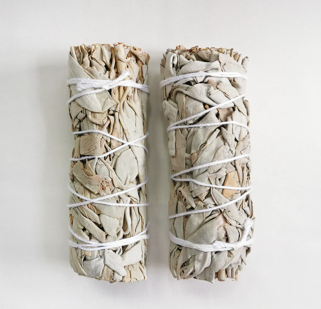 Two rolled up white sage sticks secured with white string on a light background.