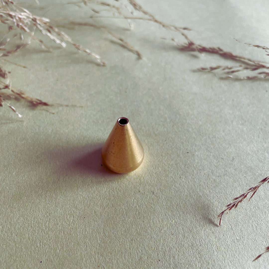 A gold-colored brass incense holder placed on a beige surface with dried plant fronds around it.