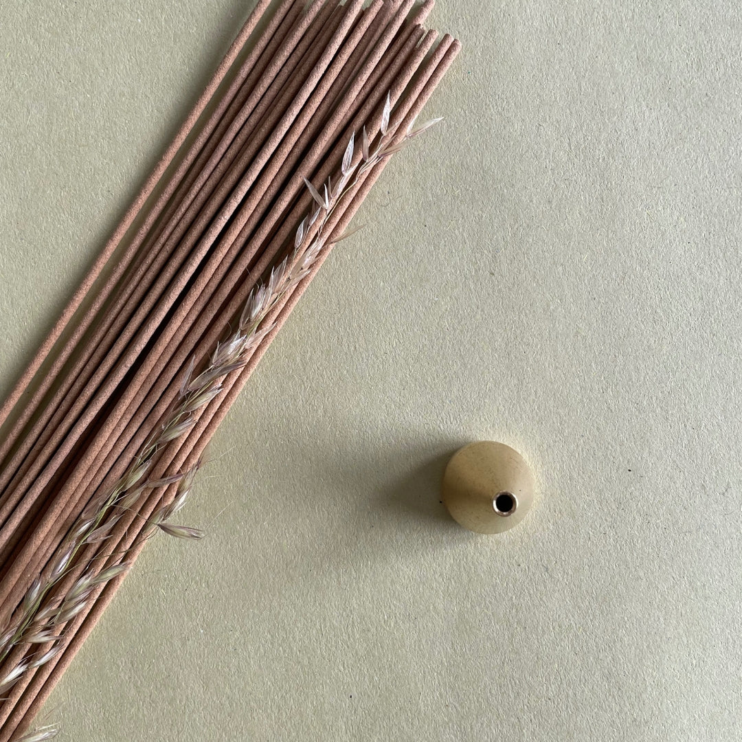 Natural sandalwood incense sticks placed next to incense holder against a light colour background