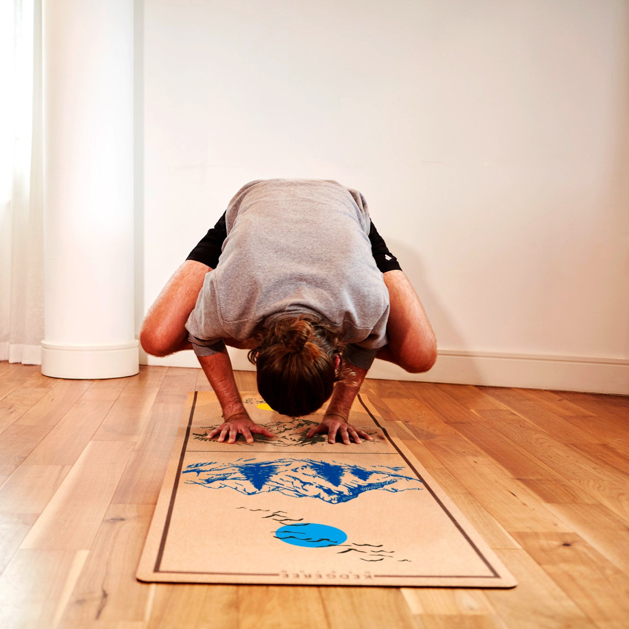Man practicing advanced yoga pose on sustainable cork yoga mat with mountain landscape and sun artwork – durable and supportive mat