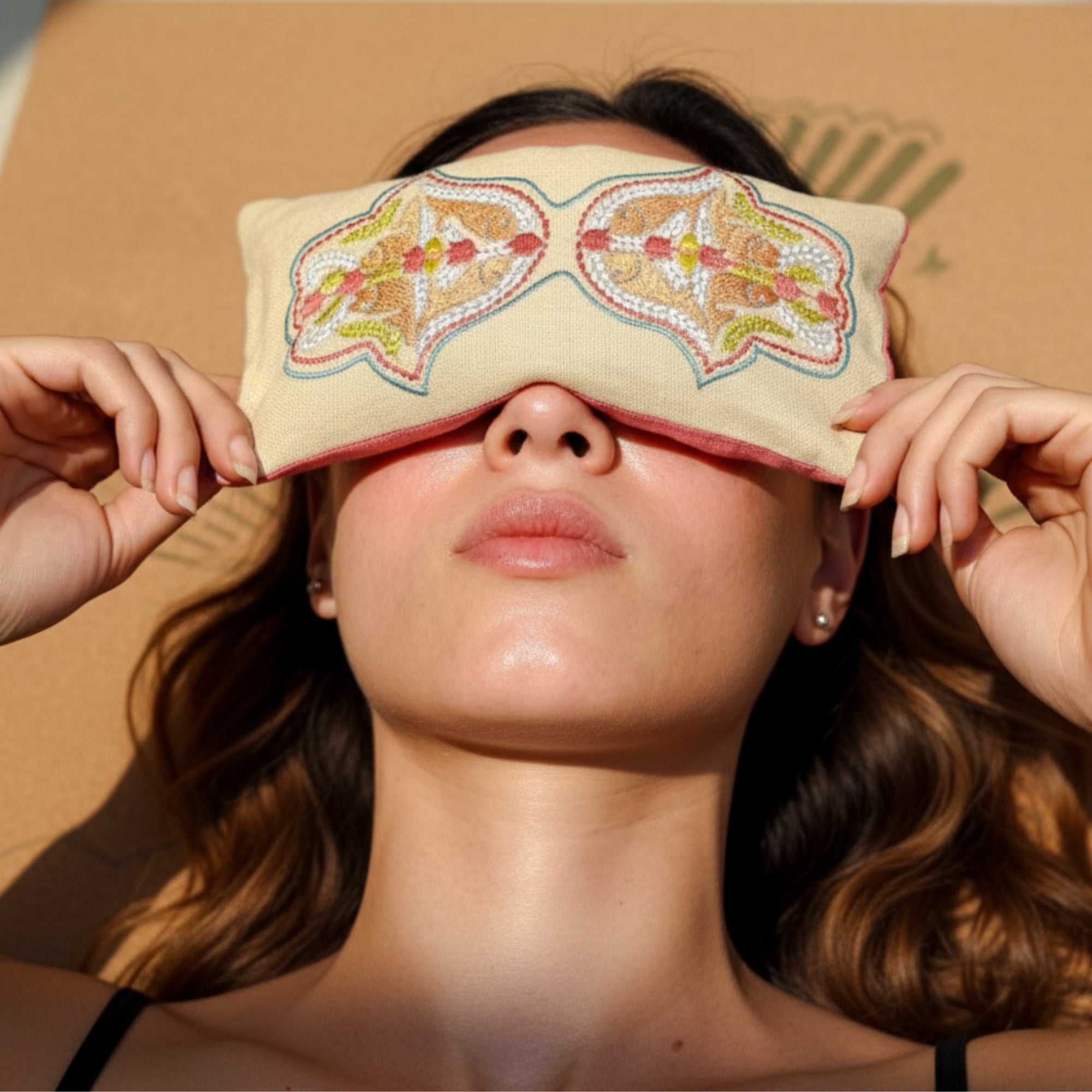 Woman wearing a kedgeree eye pillow on a cork yoga mat against a brown background