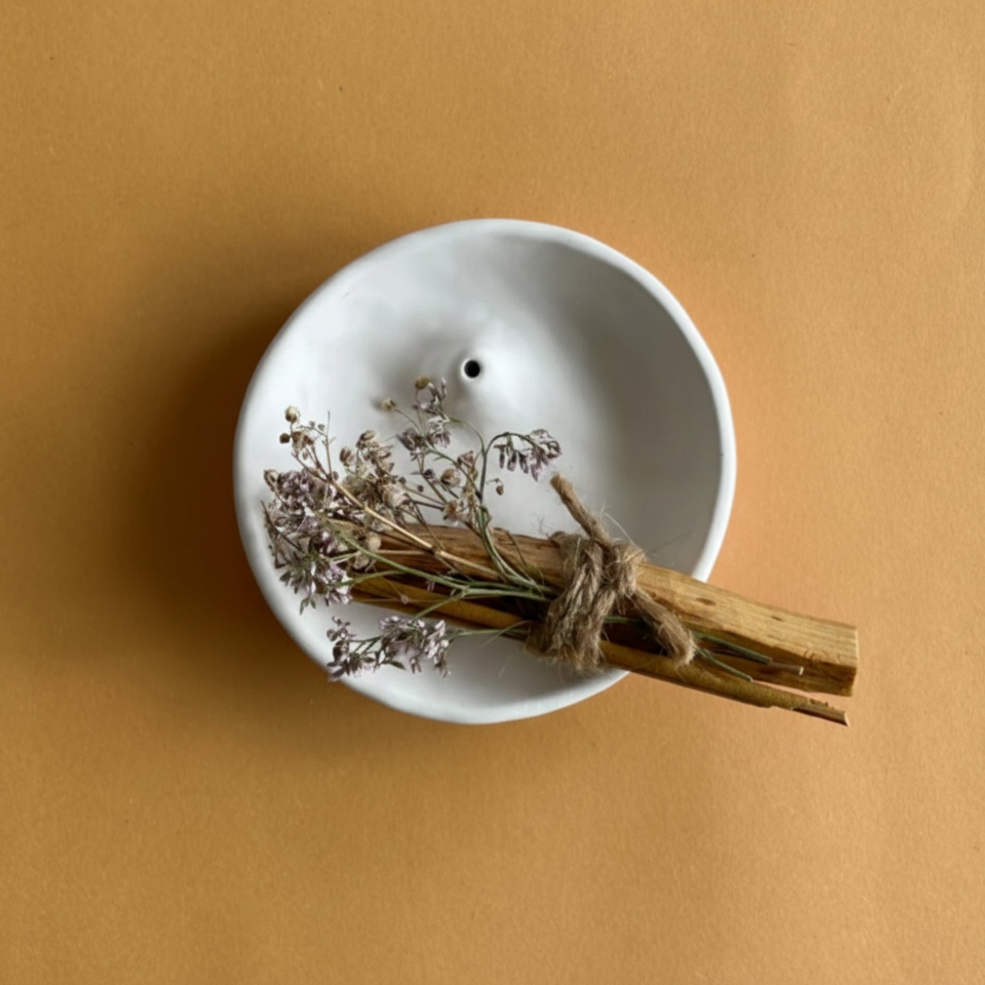 White ceramic bowl shaped incense holder and palo santo burner on a mustard yellow background