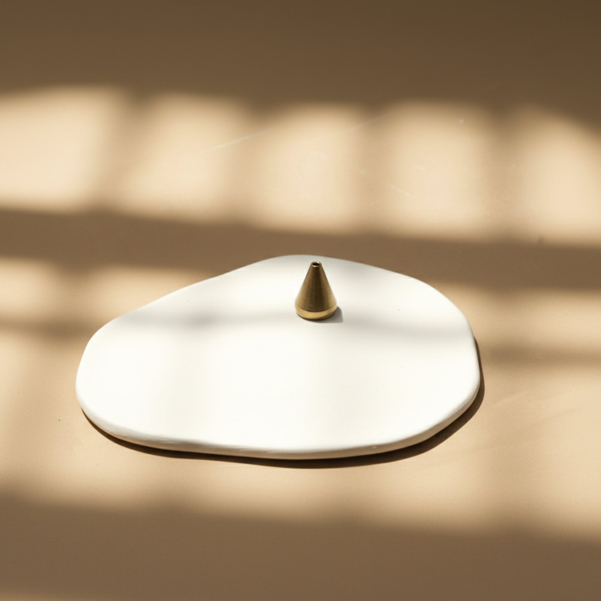 White ceramic plate with a gold water drop incense holder on a beige surface