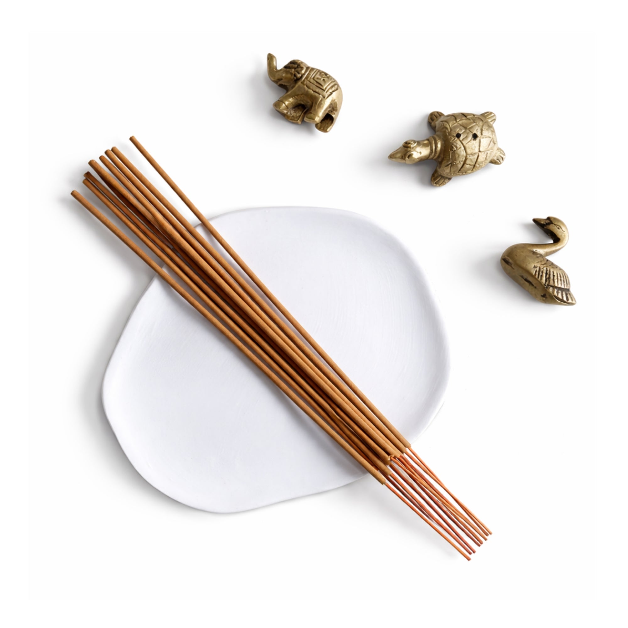 Sandalwood incense sticks on a white ash catcher tray with decorative handmade brass animal figurines incense holder  on a brown background