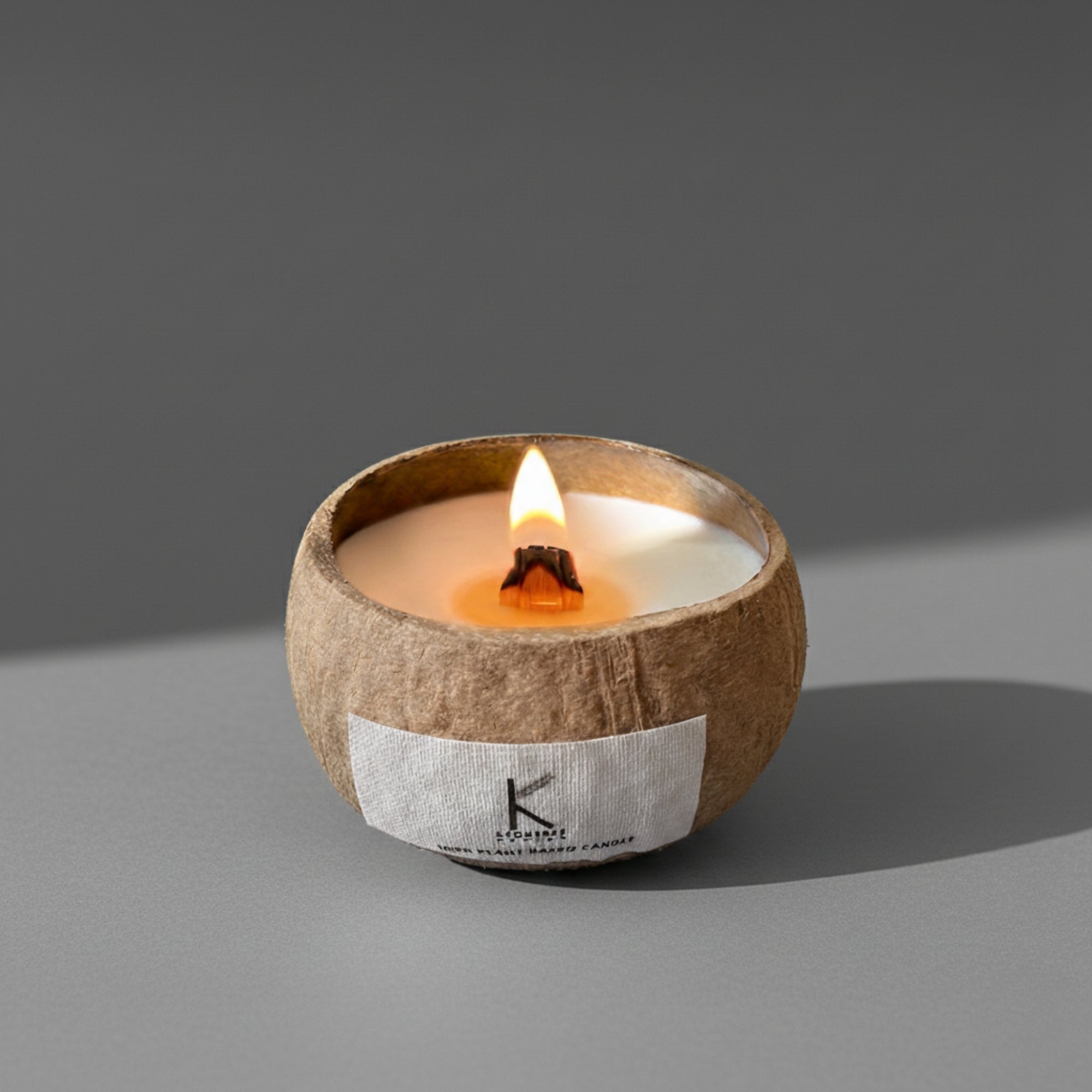 Plant based candle in a coconut shell with a visible brand label on a gray background