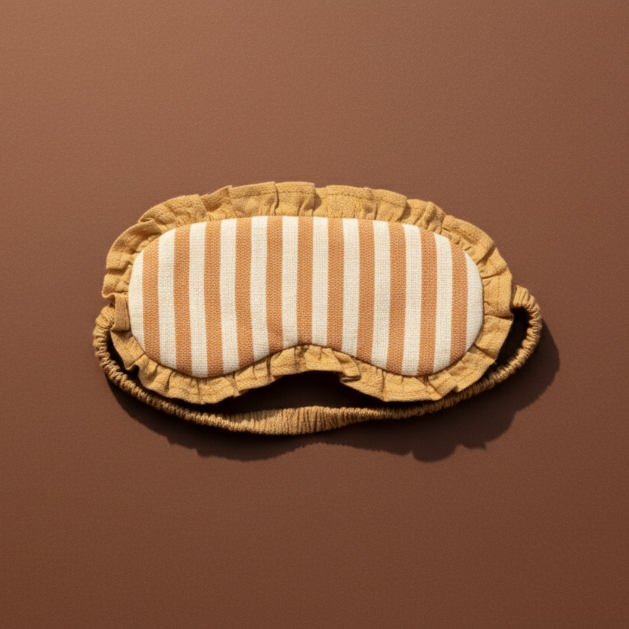 Striped yoga linen eye mask with mustard yellow border on a brown background
