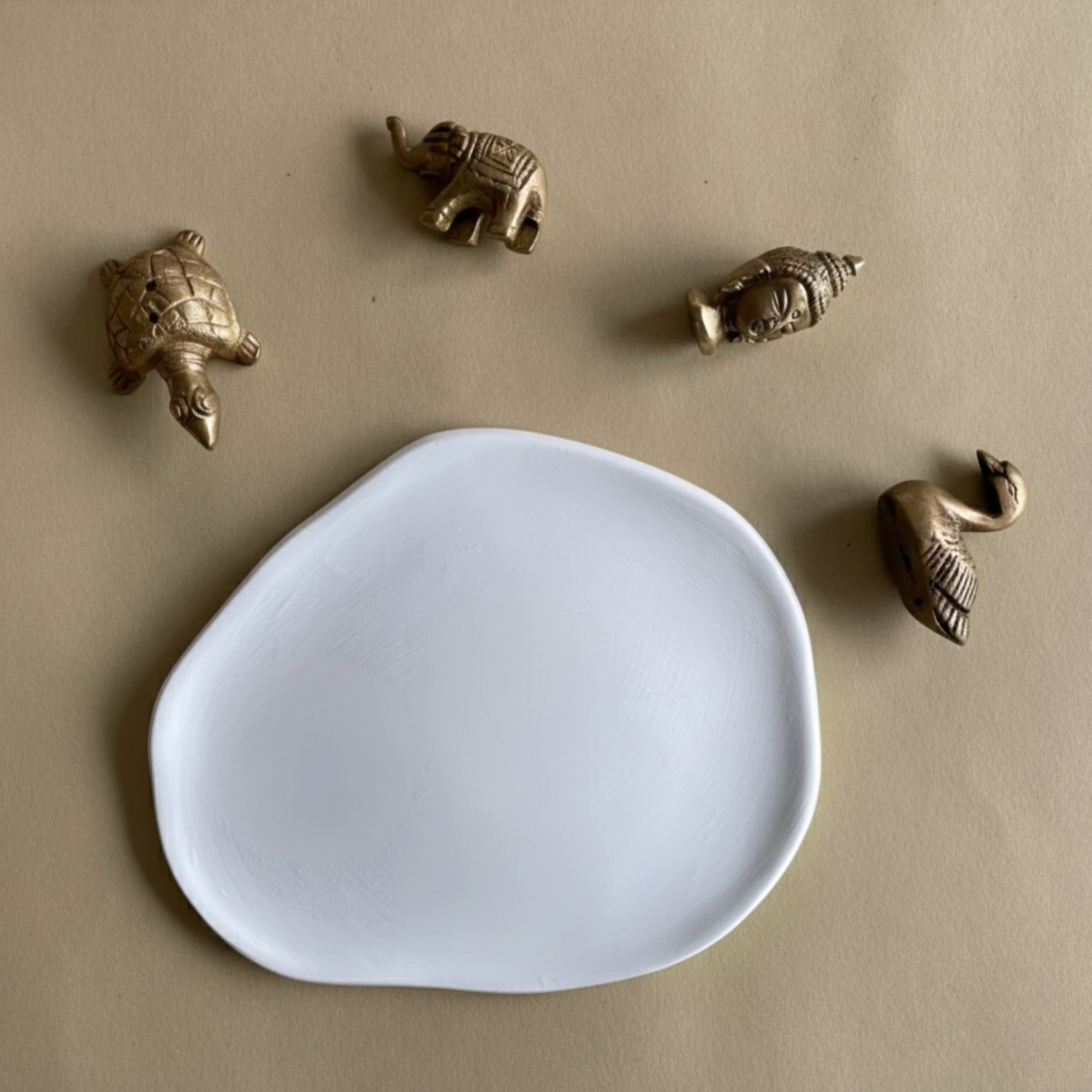 White plate on a beige background with small brass animal figurines incense holder.