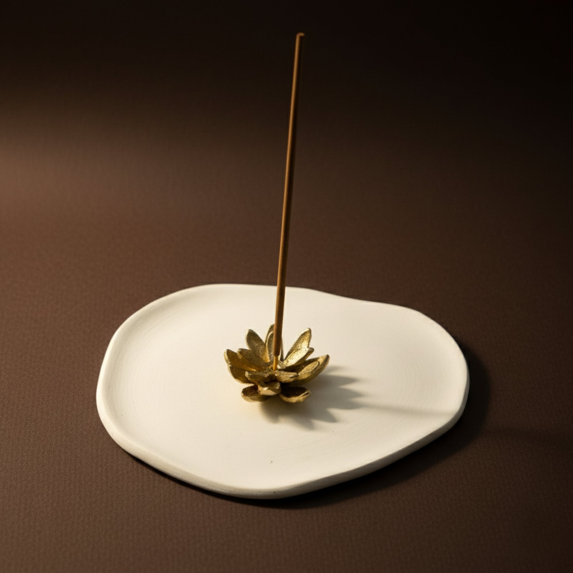 Gold lotus handmade brass  incense stick holder on a white ash catcher tray with a brown background