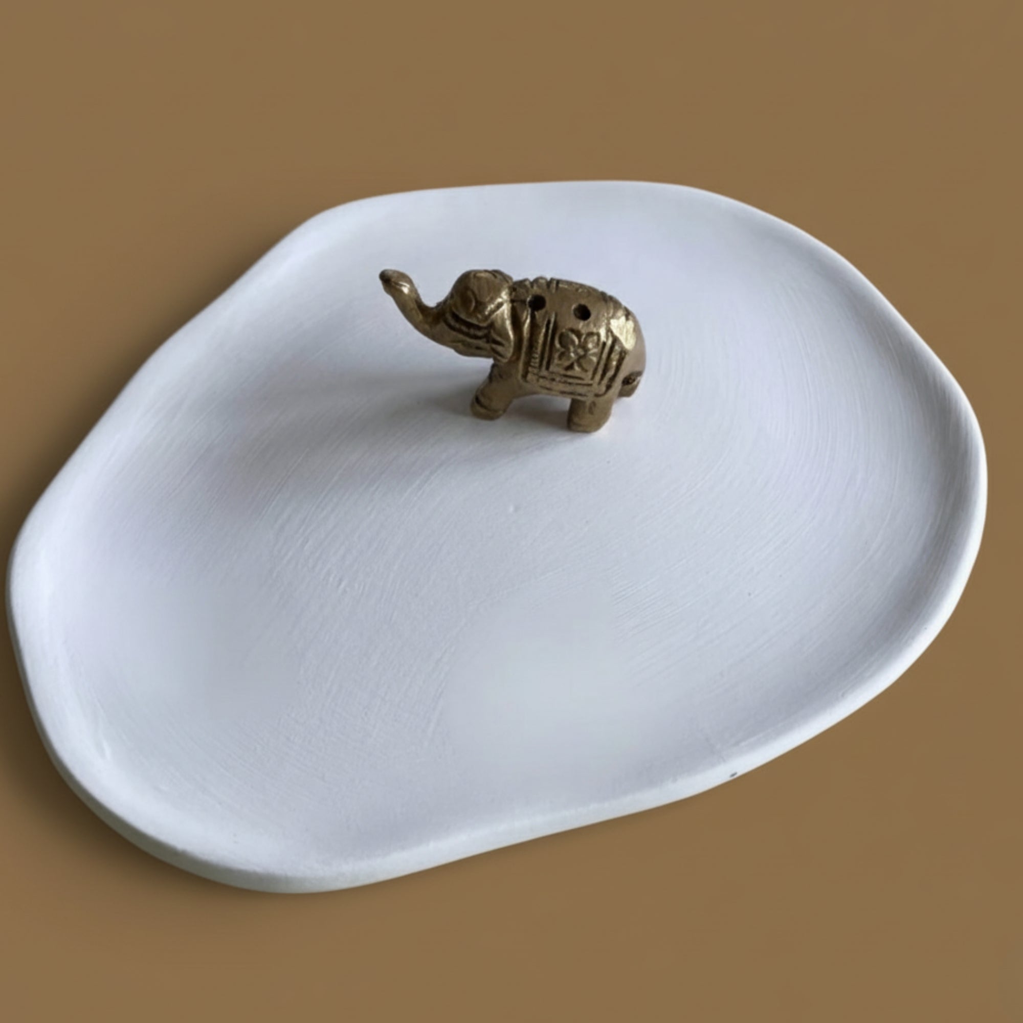 White ceramic dish with a brass elephant figurine incense holder on a brown background