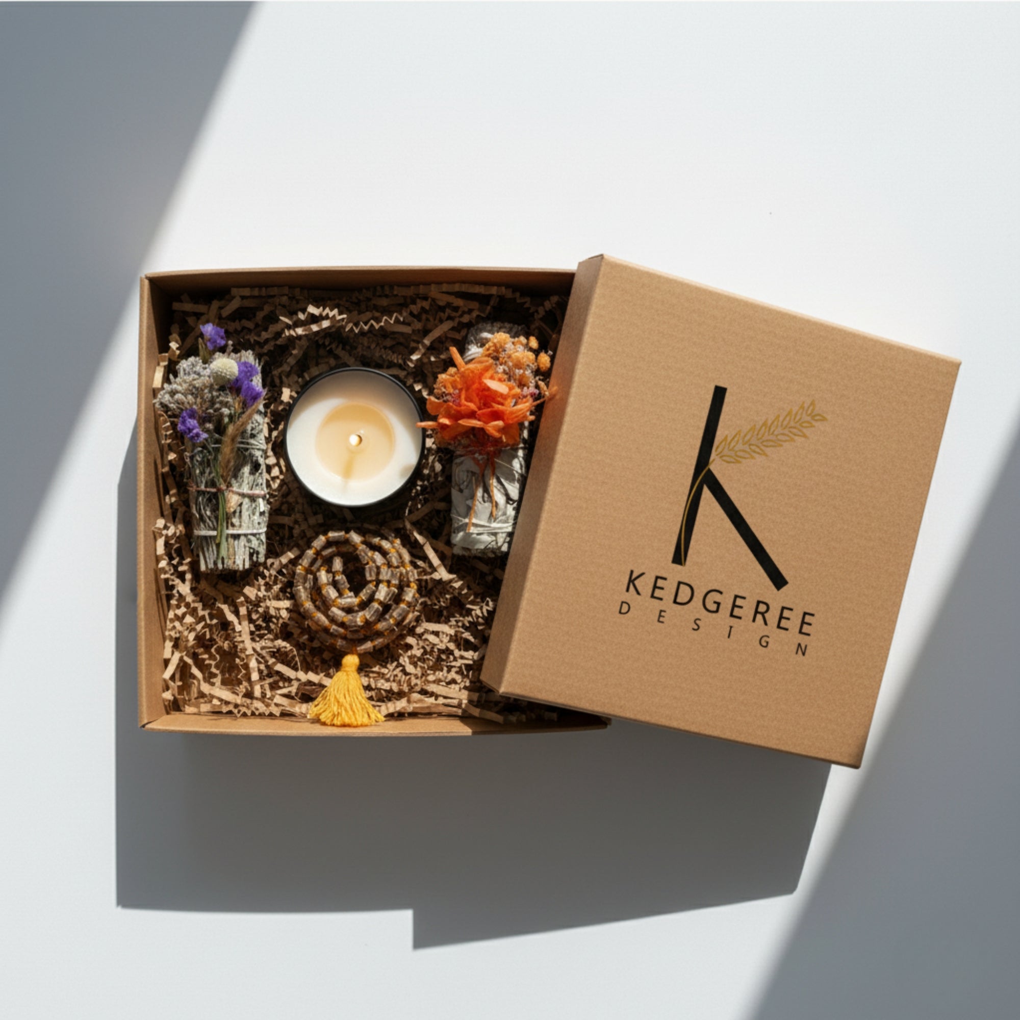 Gift box with a candle, 2 set of white sage, and a mala  featuring Kedgeree Design logo.