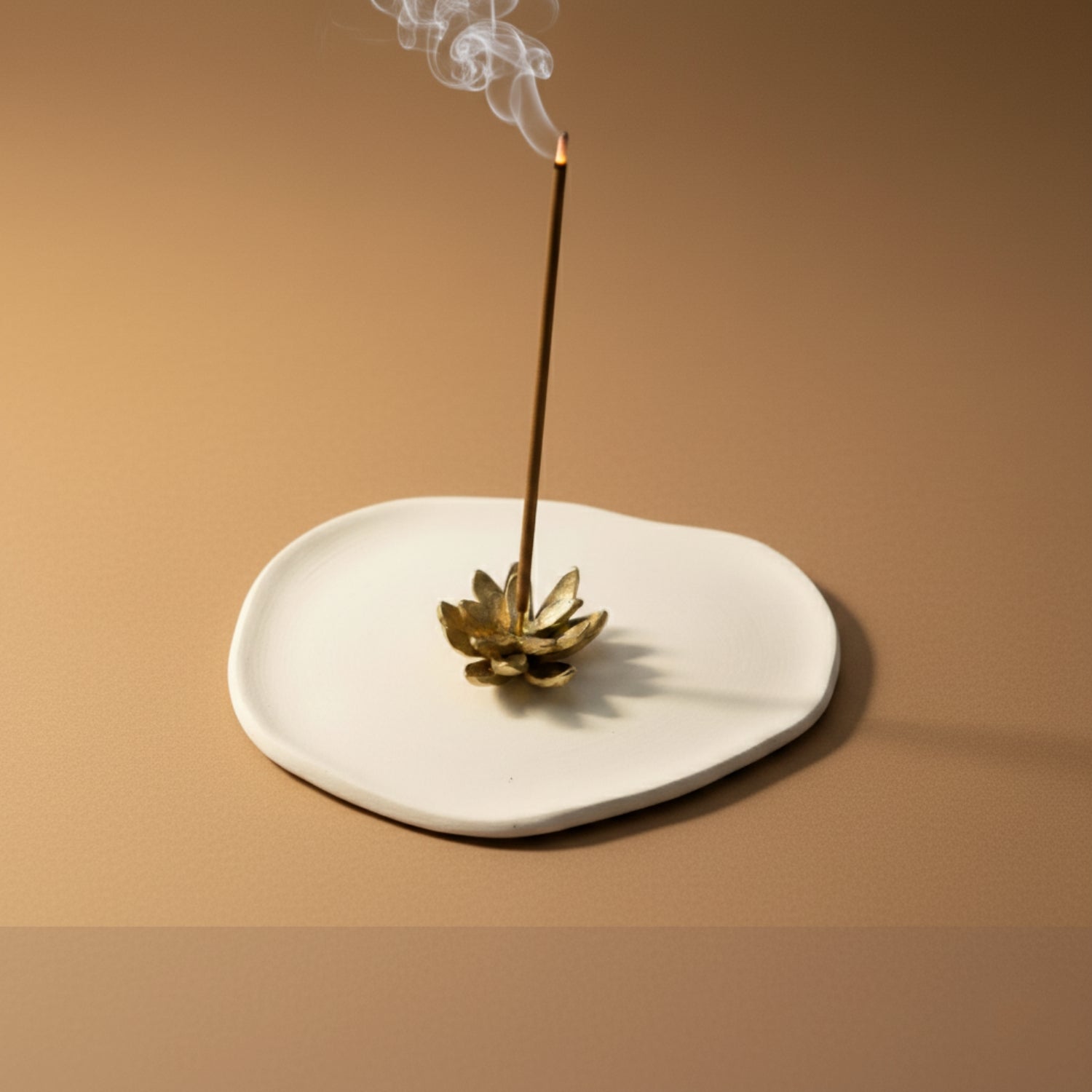 Incense stick with a decorative premium brass holder on a beige plate against a beige background