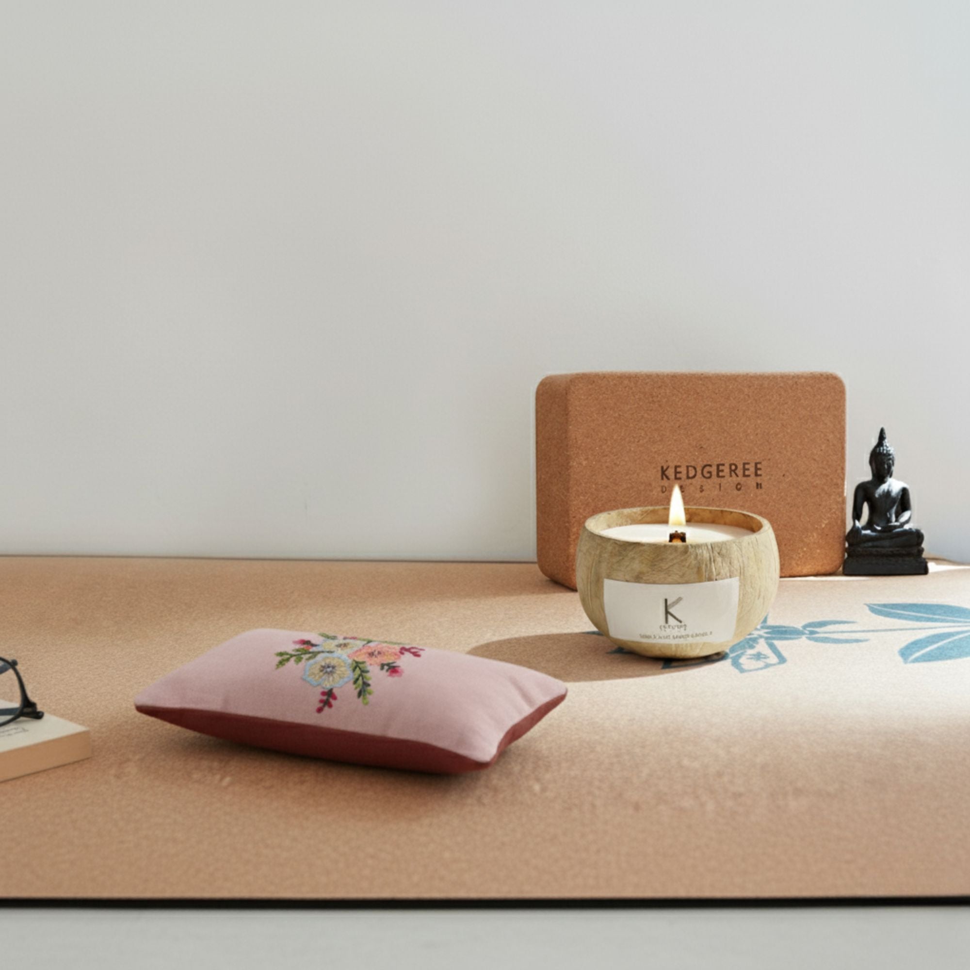 Plant based coconut shell Candle with a lit flame, decorative eye  pillow, and Buddha statue on a surface with a neutral background