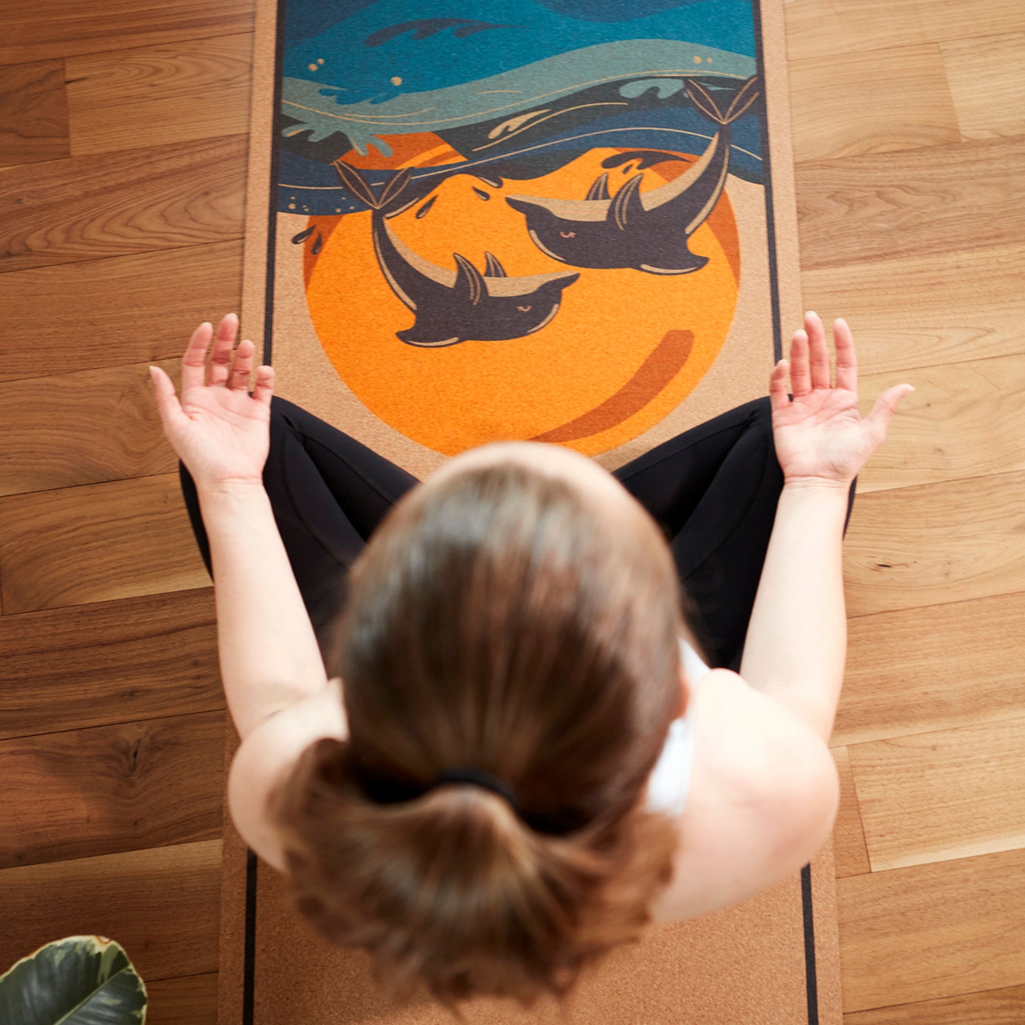 Woman meditating on eco-friendly cork yoga mat with dolphin and sunset ocean design – non-slip surface for mindfulness and yoga practice.