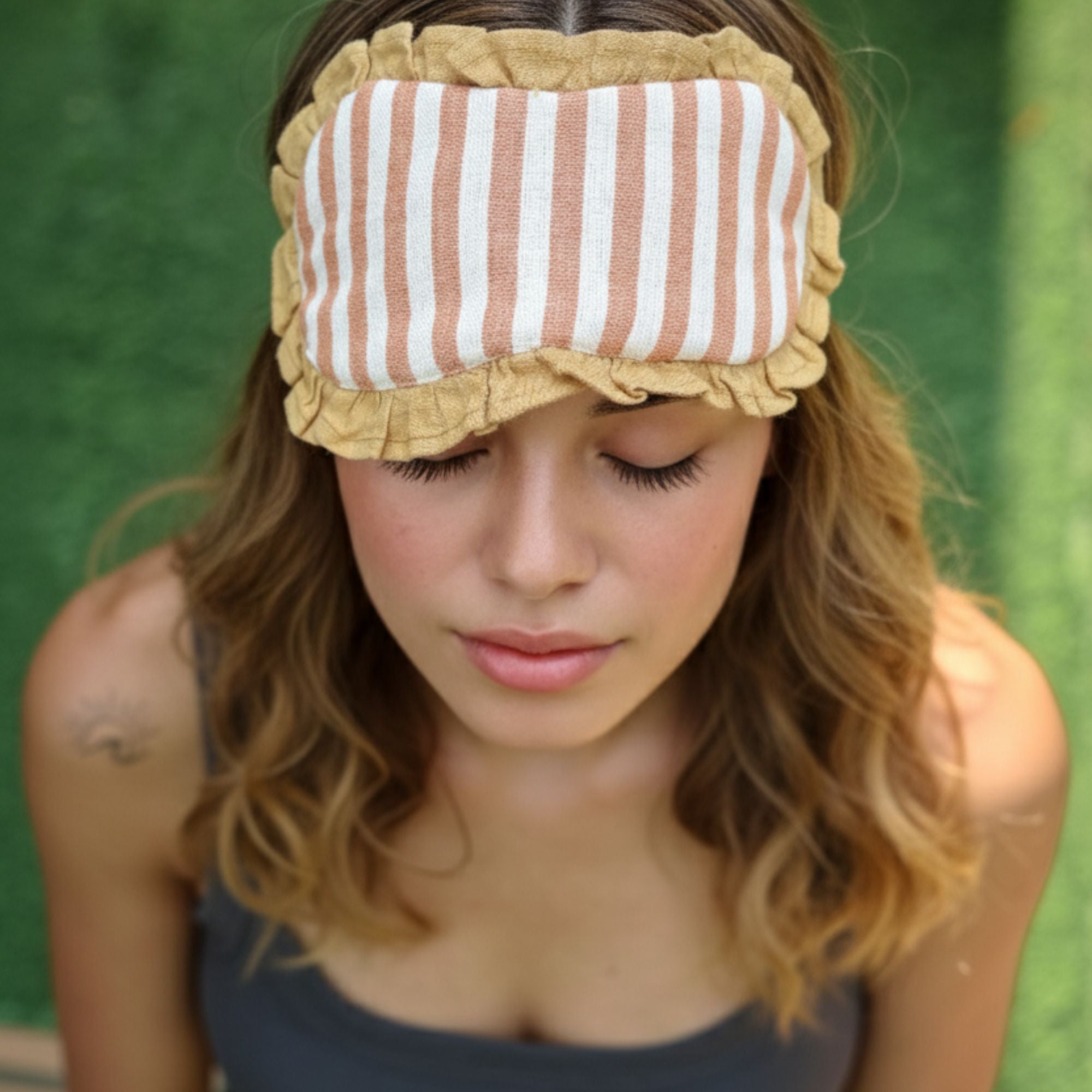 Woman wearing a striped linen eye mask with ruffles against a green background