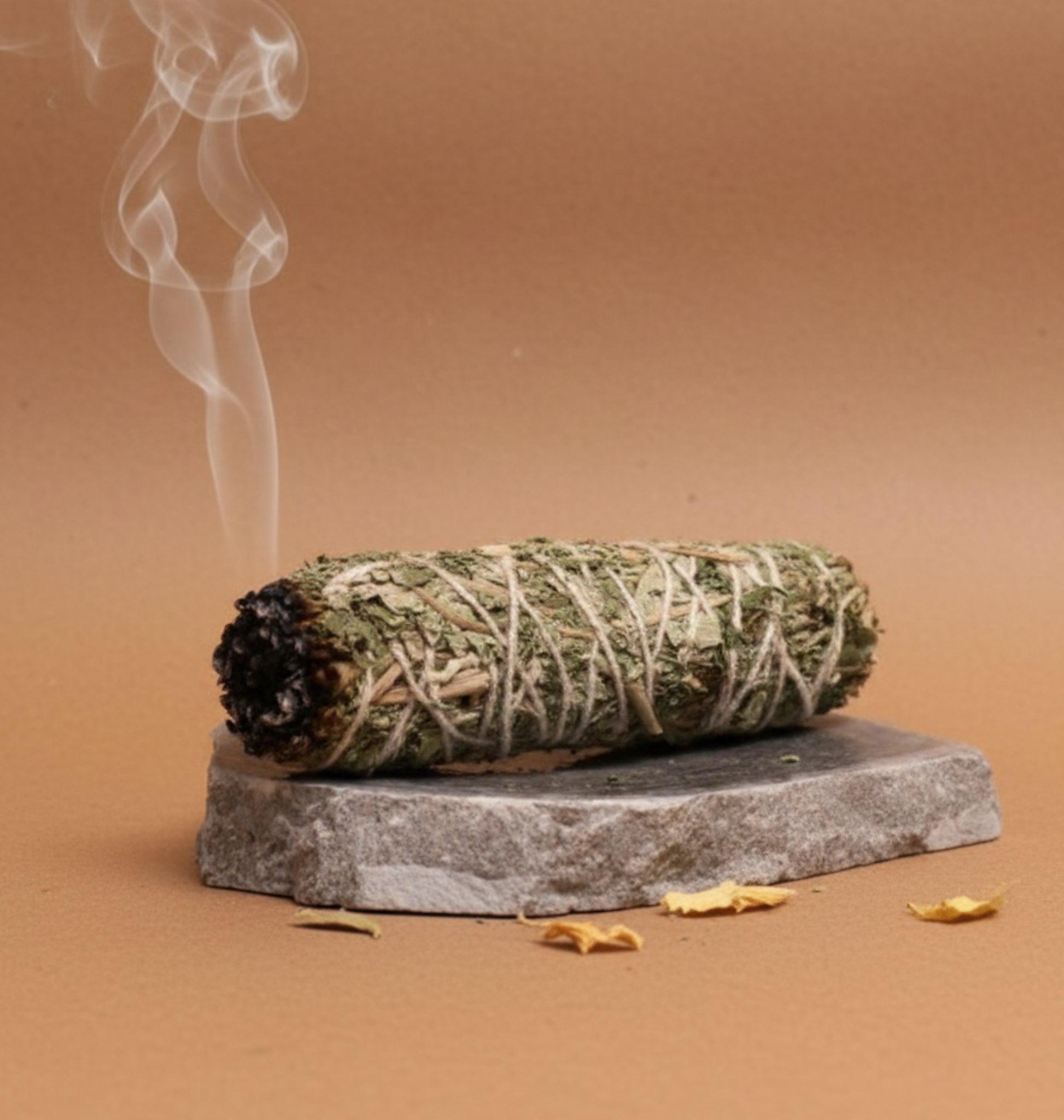 Smoldering white indian sage bundle on a stone platform with a brown background