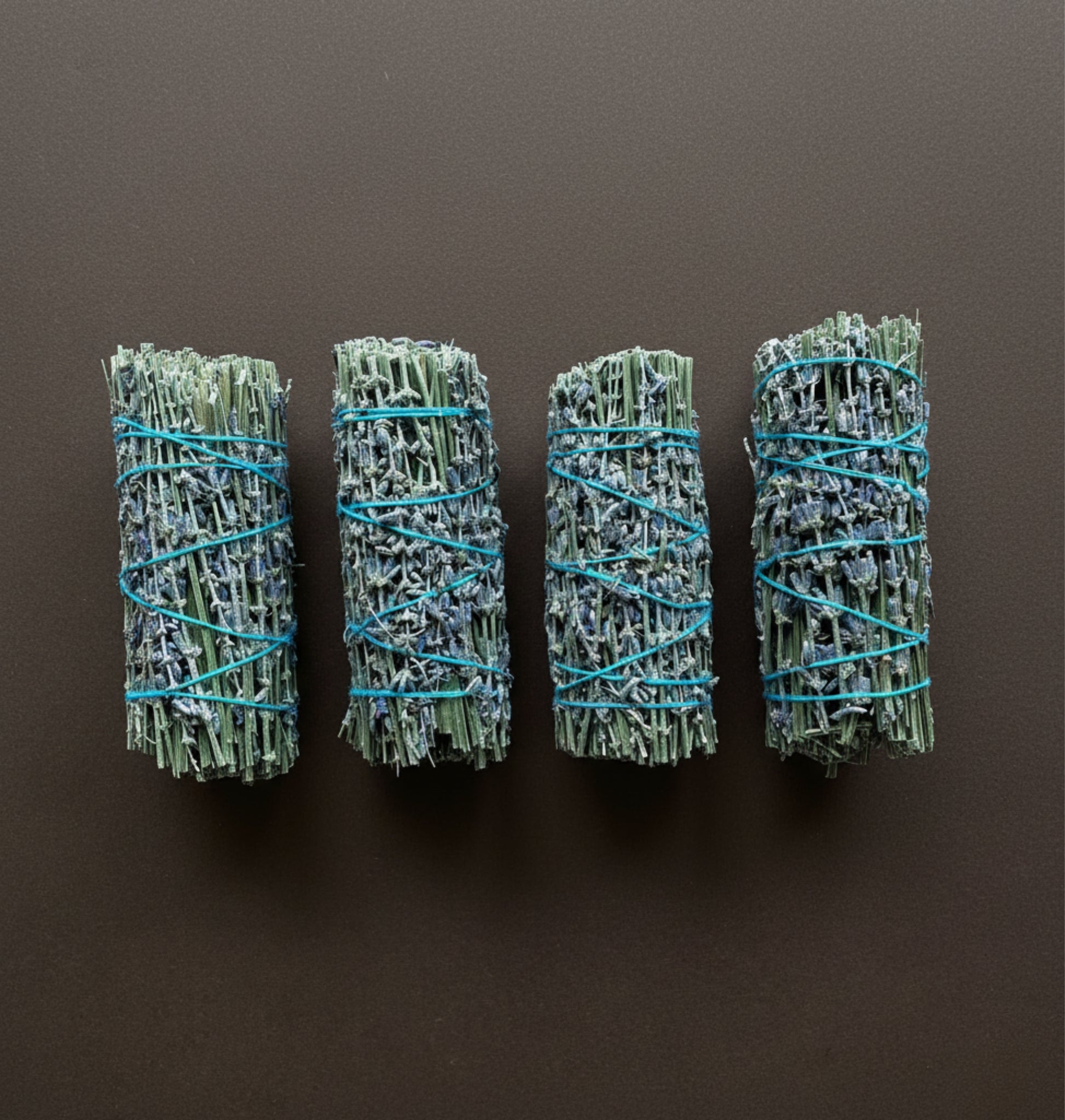 Four bundles of natural lavender smudge sticks tied with blue string on a dark background