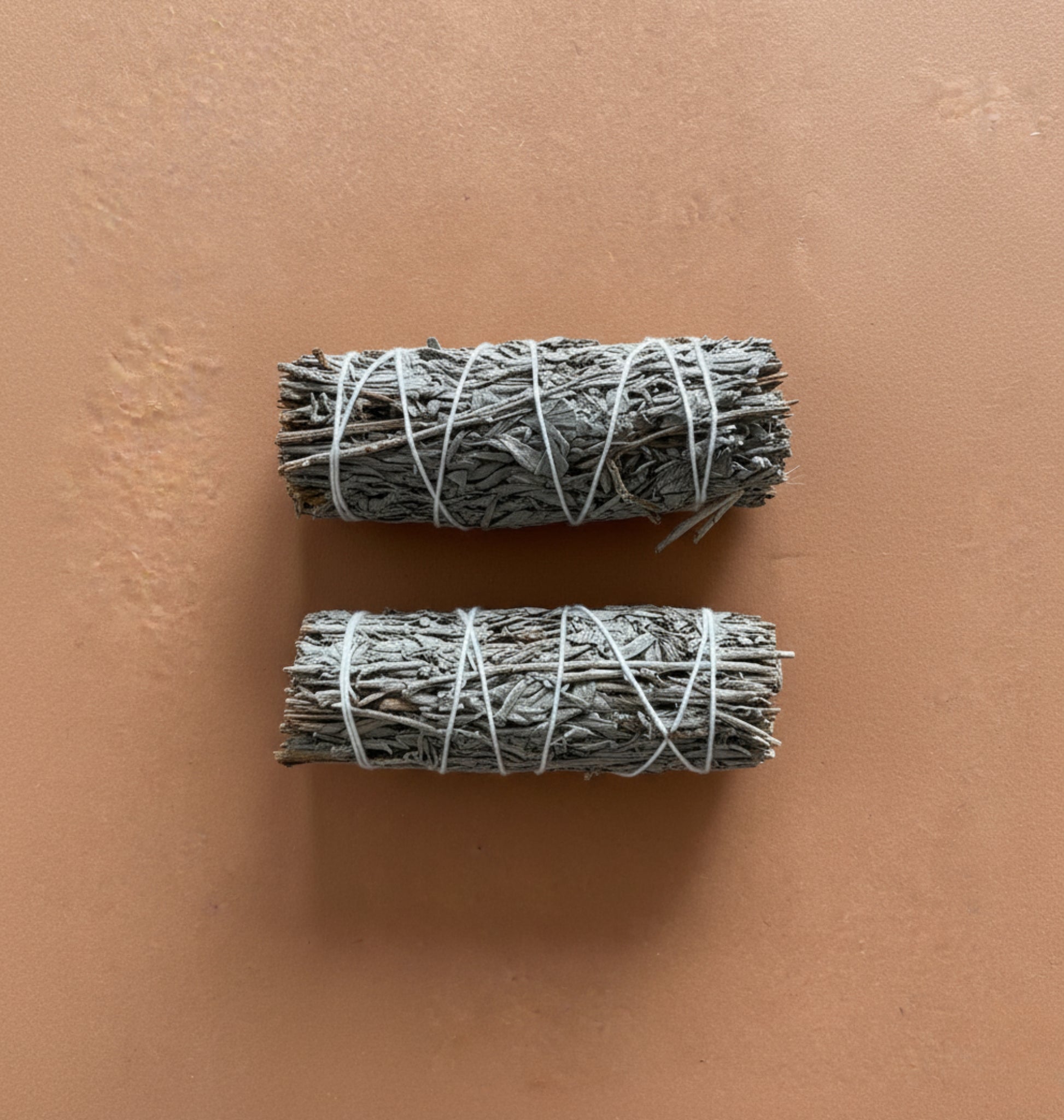 Two bundles of natural blue sage wrapped in twine on a brown background