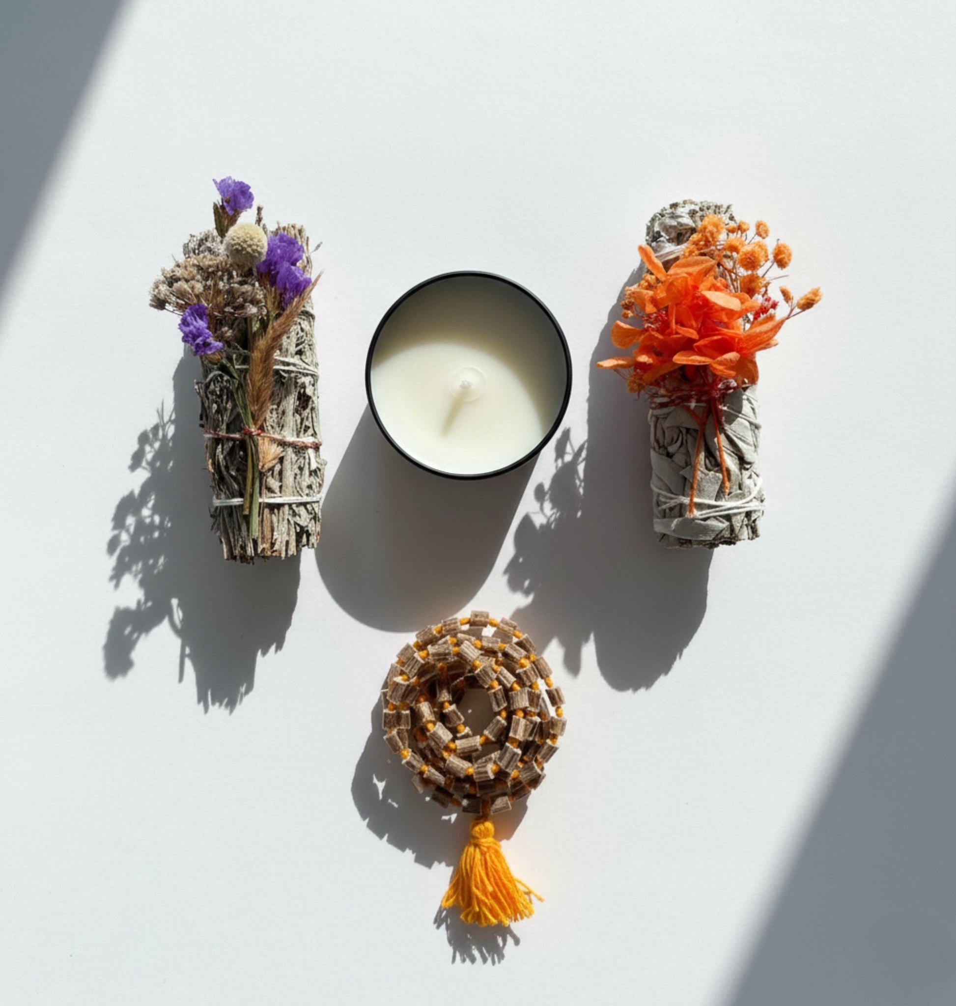 A gift set that includes blue smudge, white smudge, plant based candle, and beads mala on a white surface.