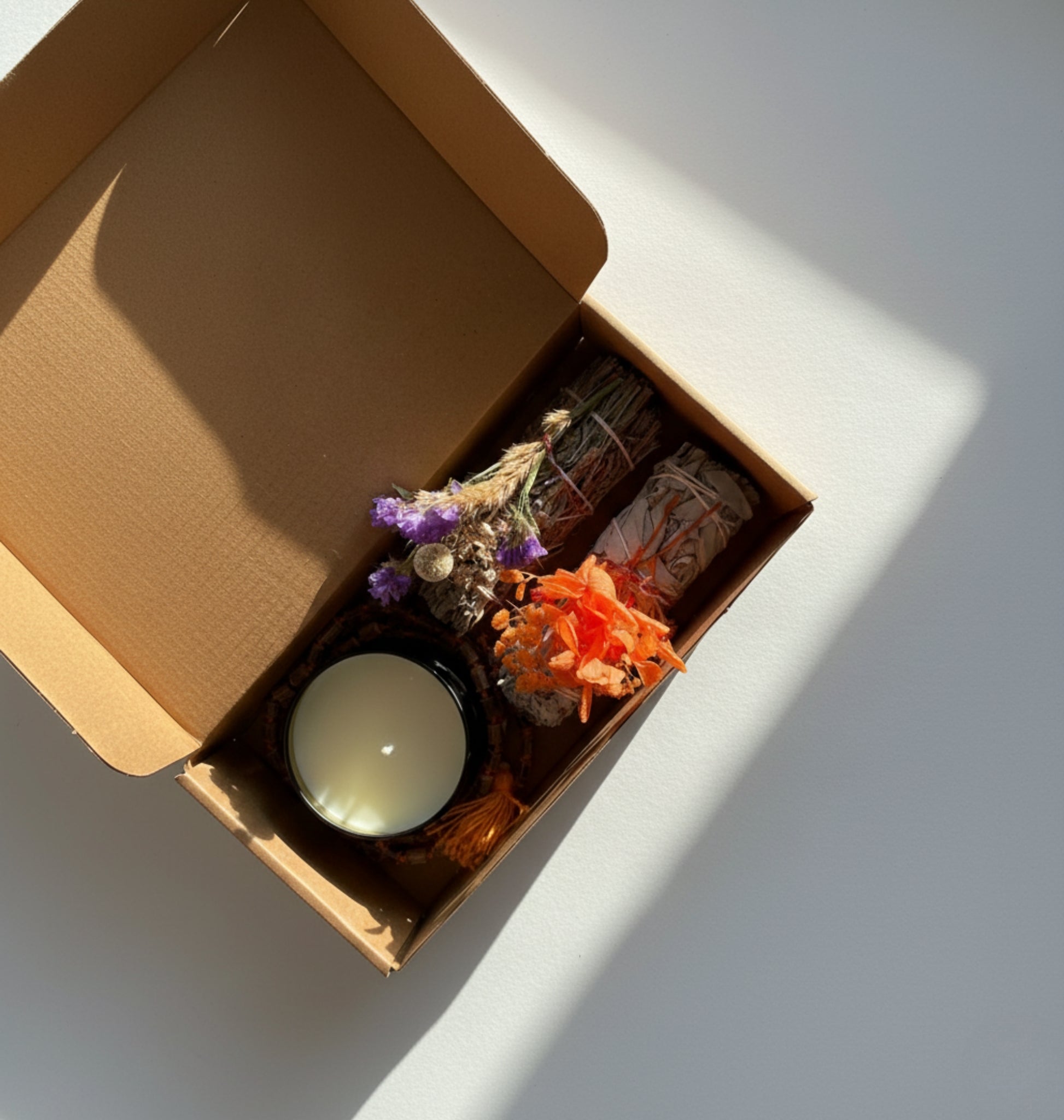 A gift set that includes blue smudge, white smudge, plant based candle, and beads mala decorated with naturally dried flowers on a white surface.