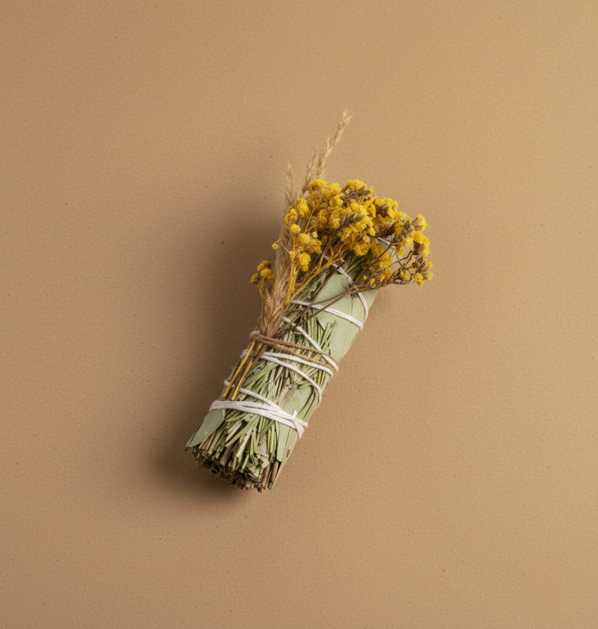 Natural Eucalyptus Rosemary Smudge Bundled yellow flowers tied with twine on a brown background