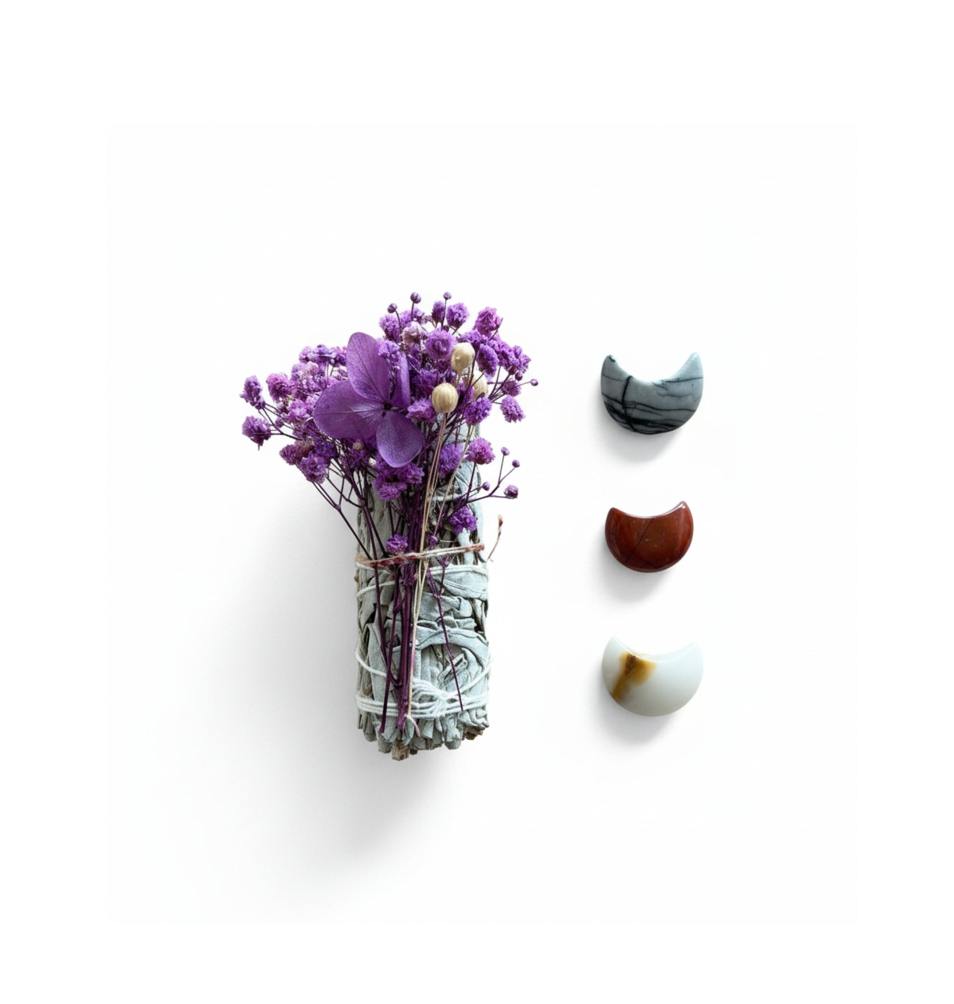 A bundle of white sage with purple flowers and three decorative stones on a white background